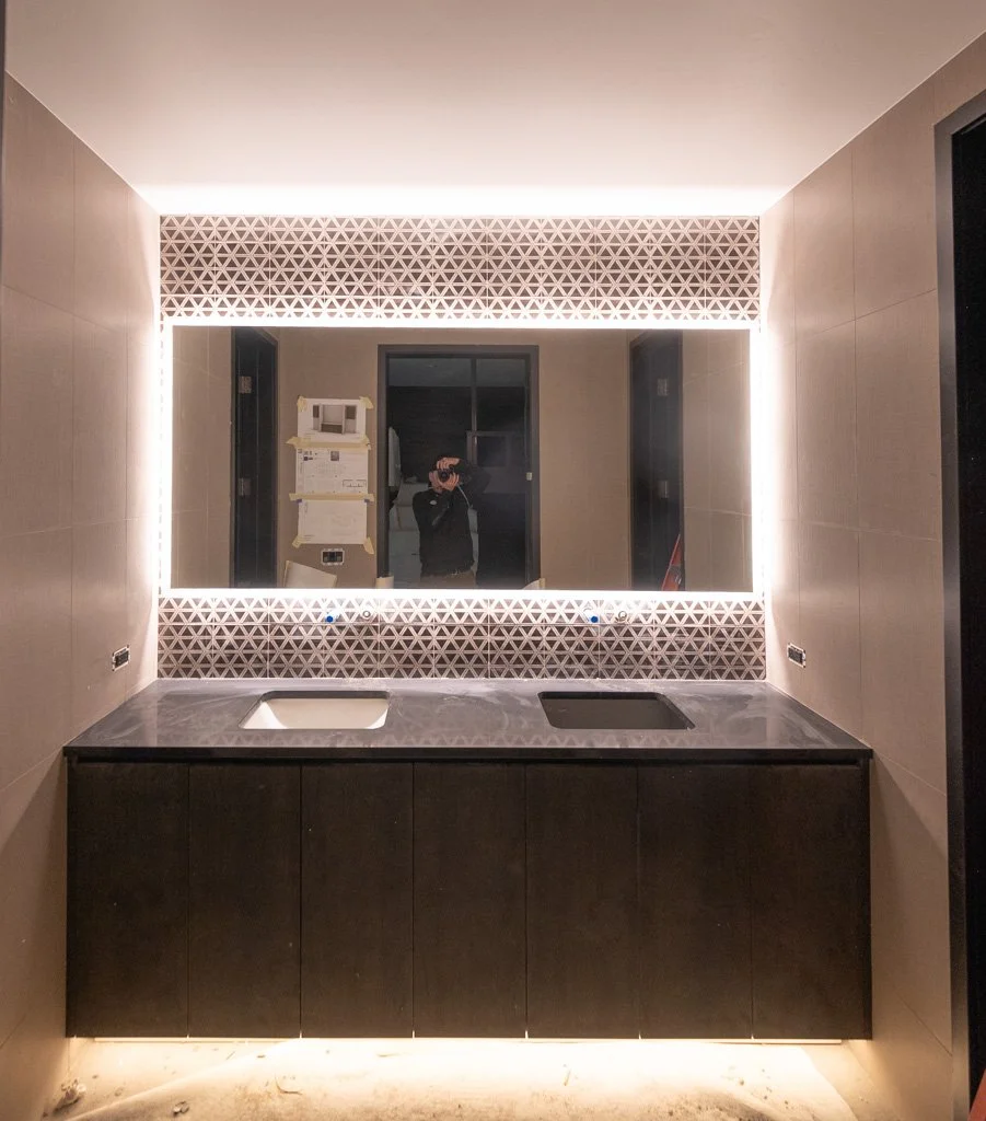 Modern bathroom vanity with a large backlit mirror, a sink, and a countertop, with geometric patterned walls and soft ambient lighting.