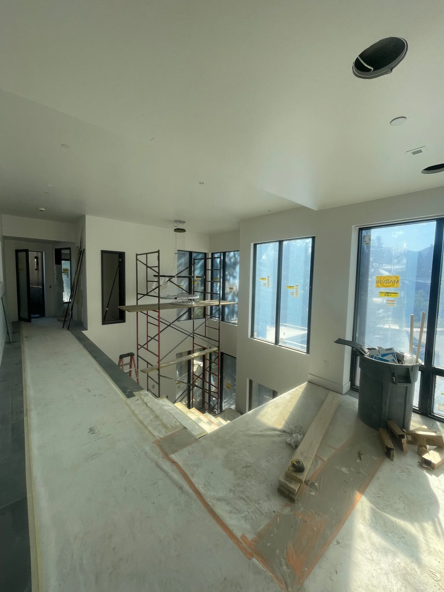 Interior of a building under construction with scaffolding, large windows, and construction tools and materials on the floor.