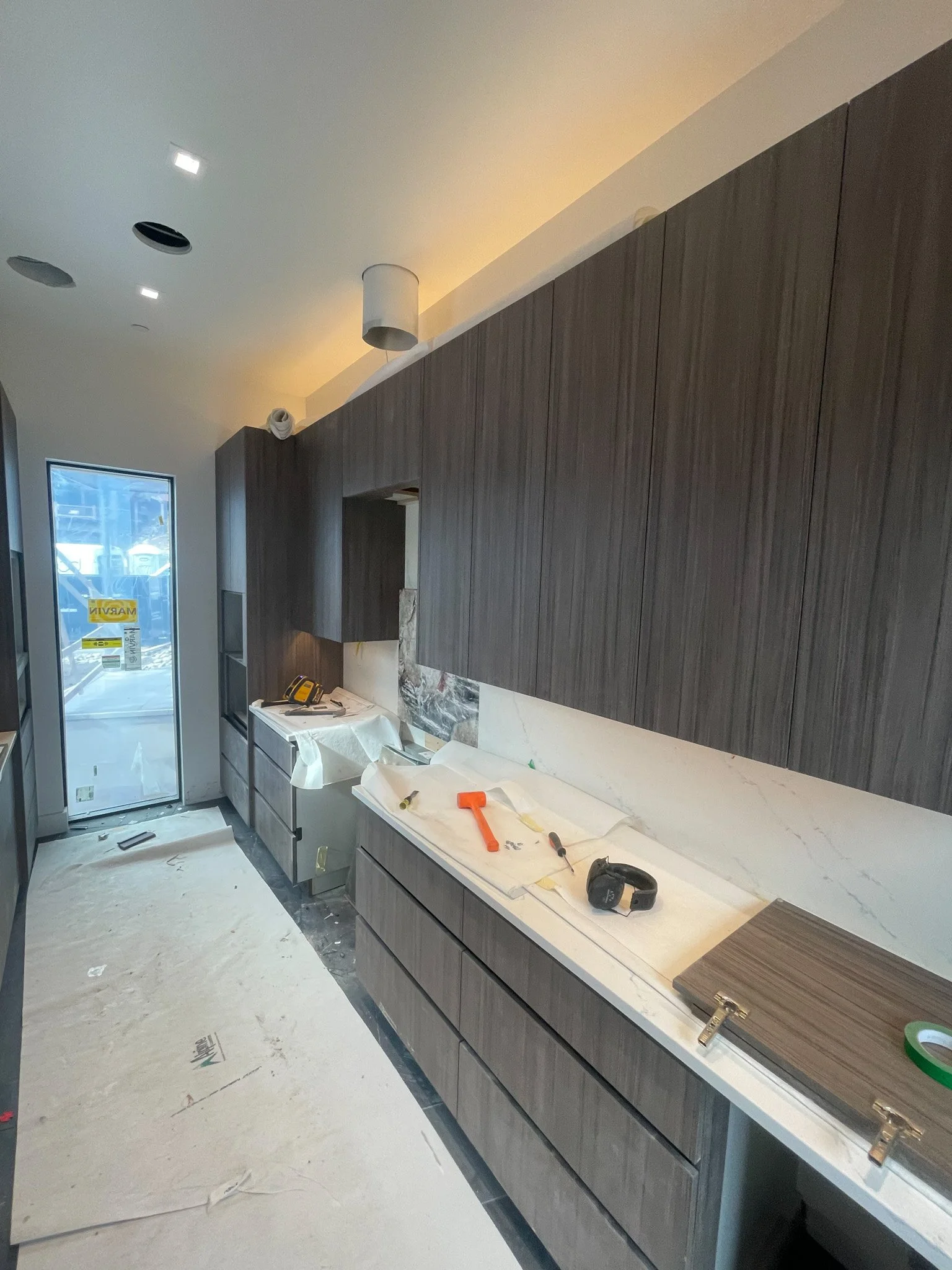 Modern kitchen under construction with dark wood cabinetry, white marble countertops, and construction tools on the counter.