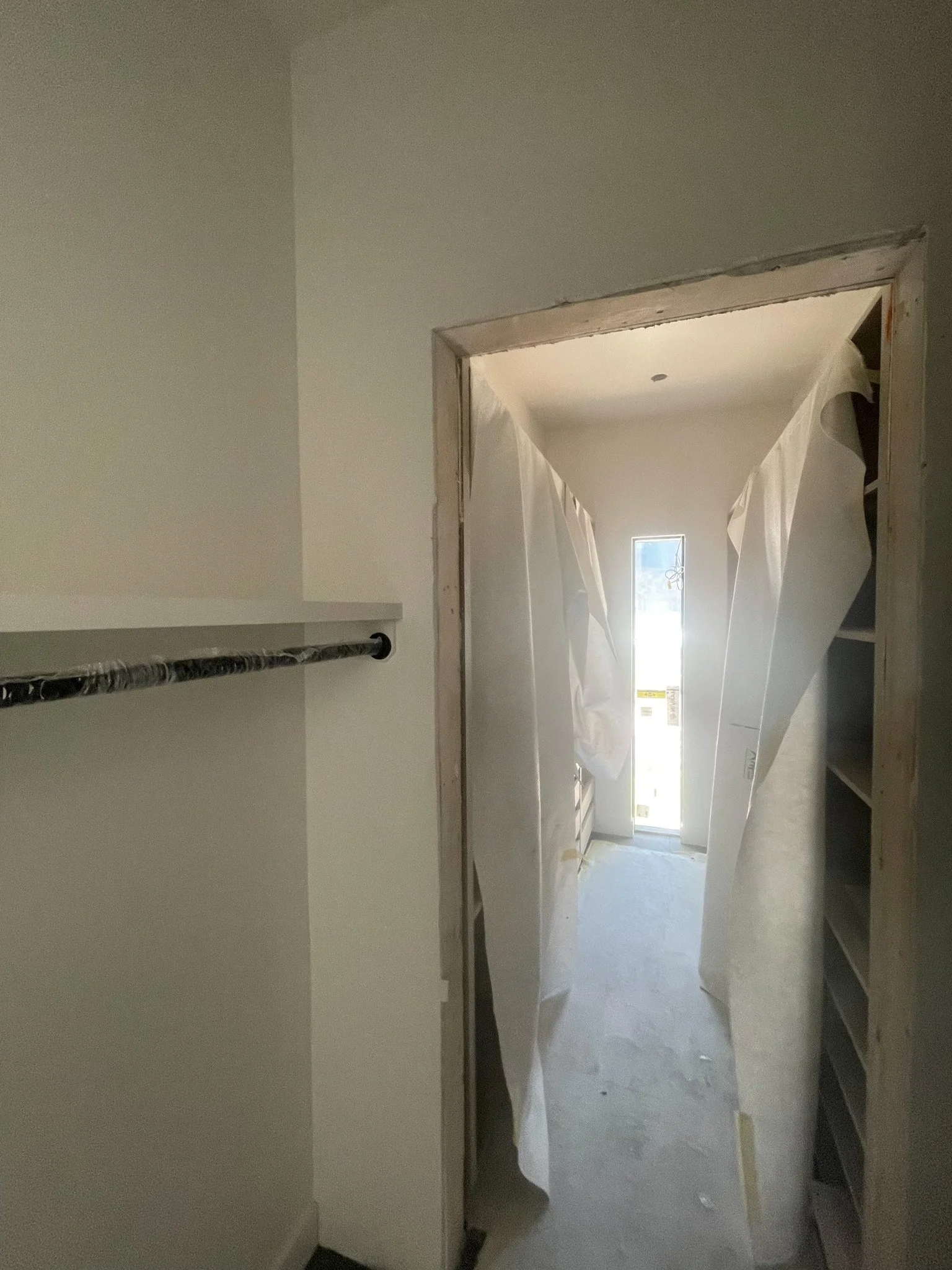 Interior view of a room under construction with a doorway covered in plastic sheeting and building materials visible inside.