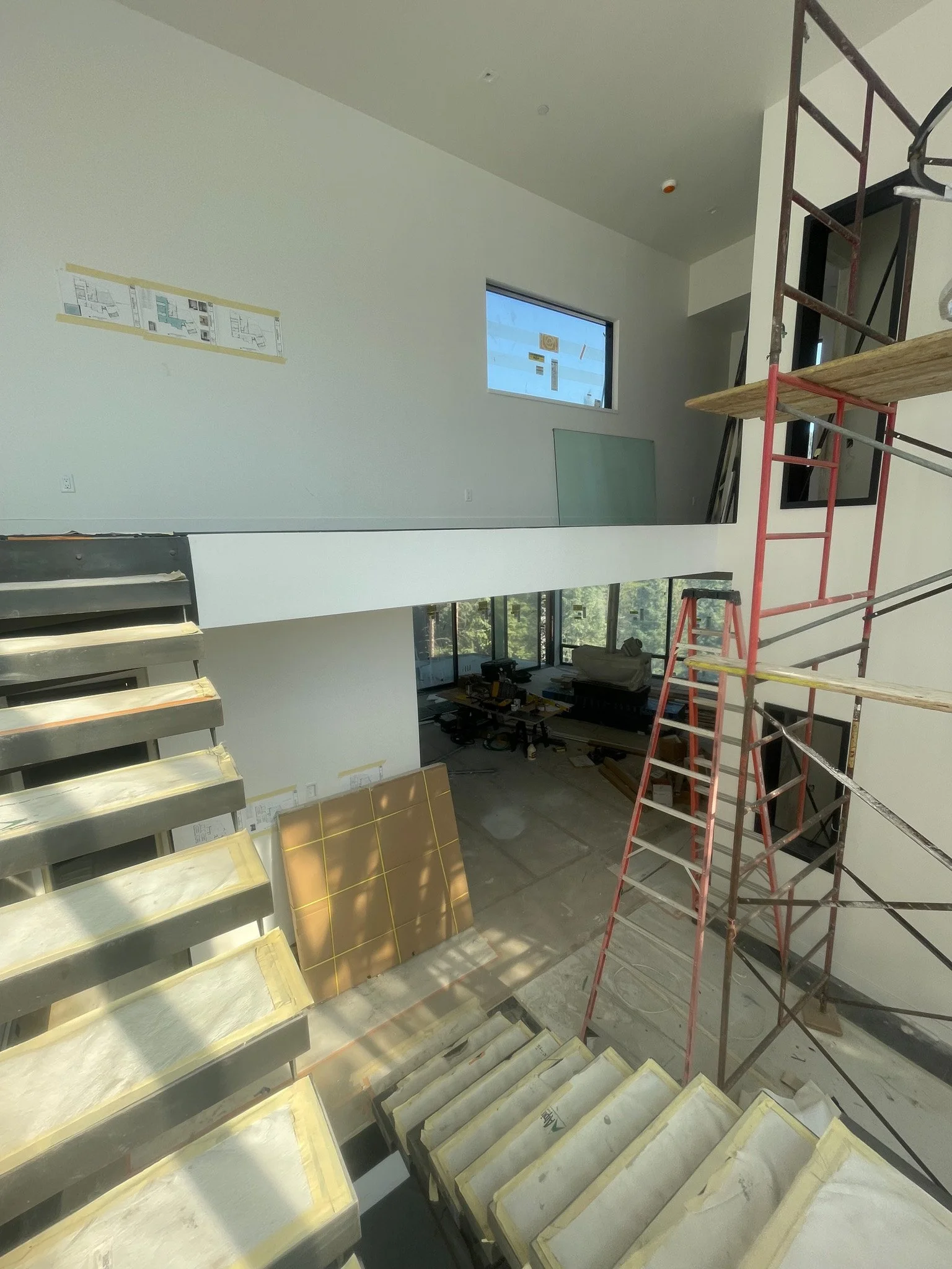 Interior view of a building under construction with stairs, scaffolding, and construction materials.