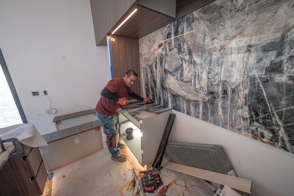 A man working on a kitchen countertop with a large marble backsplash in a kitchen under construction.