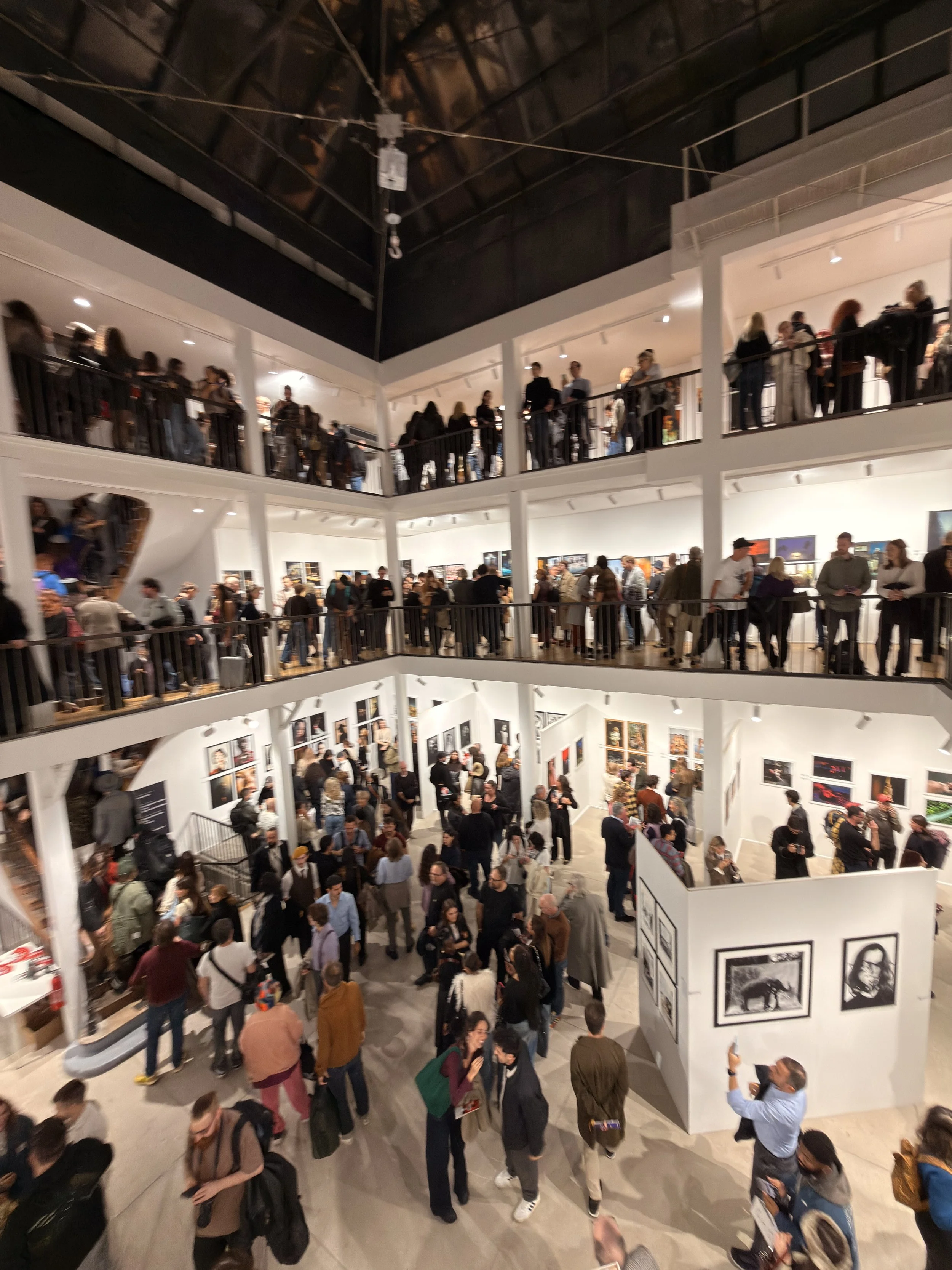 Vista di una galleria d'arte piena di visitatori che osservano opere d'arte alle pareti e nelle vetrine, con più piani e una grande apertura centrale.