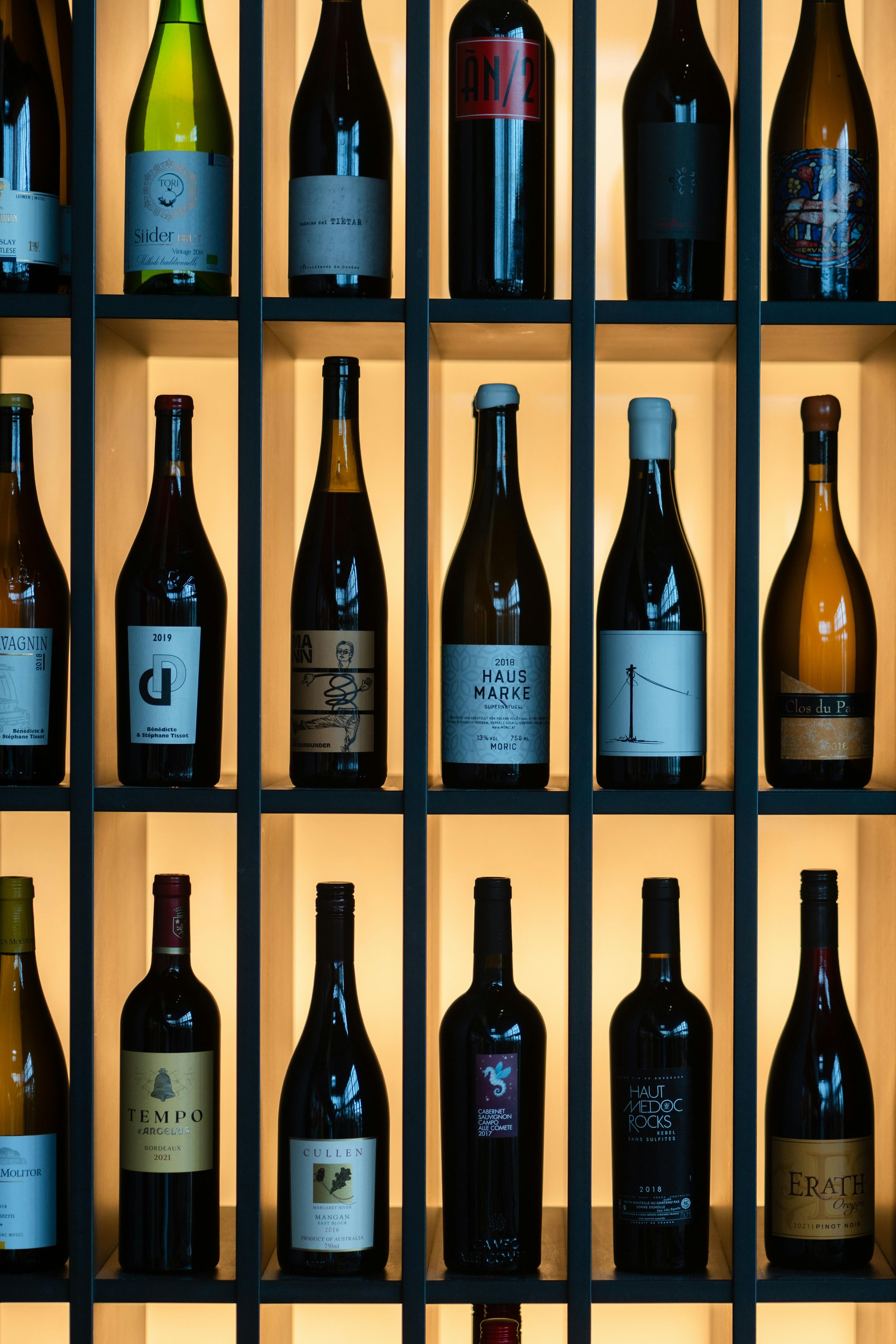 Estante con varias botellas de vino en diferentes tamaños y etiquetas, iluminadas suavemente.