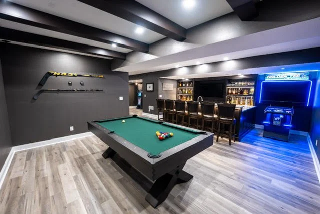 A game room with a pool table, bar area, and hockey sticks mounted on the wall.