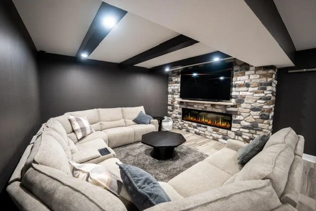 Modern living room with a stone accent wall, a fireplace, a flat-screen TV, and beige sectional sofas with pillows.