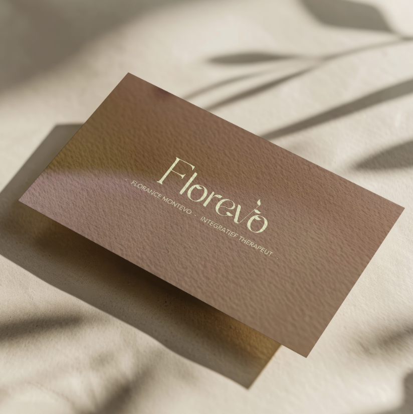 Een visittkaart met de tekst 'Florevô' en de naam 'Florence Montevo', met de titel 'Integratief Therapeut', op een beige oppervlak met schaduw en een vaag blad in de achtergrond.
