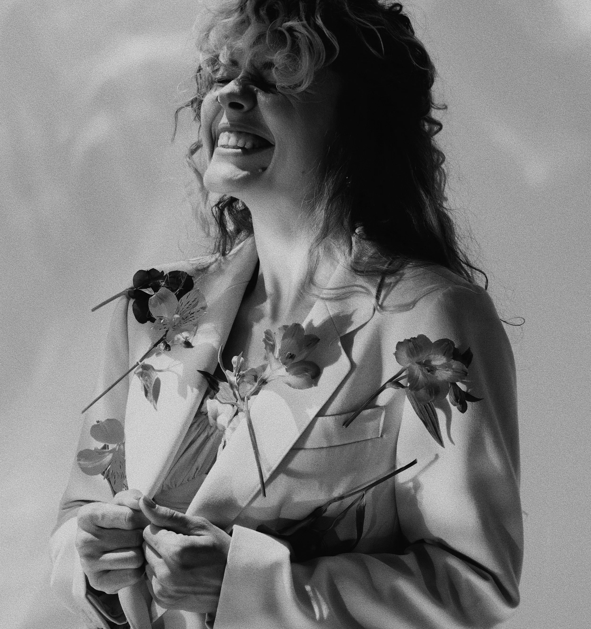 Zittend meisje met slangenhalsketting, lachend met dichtgeknepen ogen, zwart-wit foto.