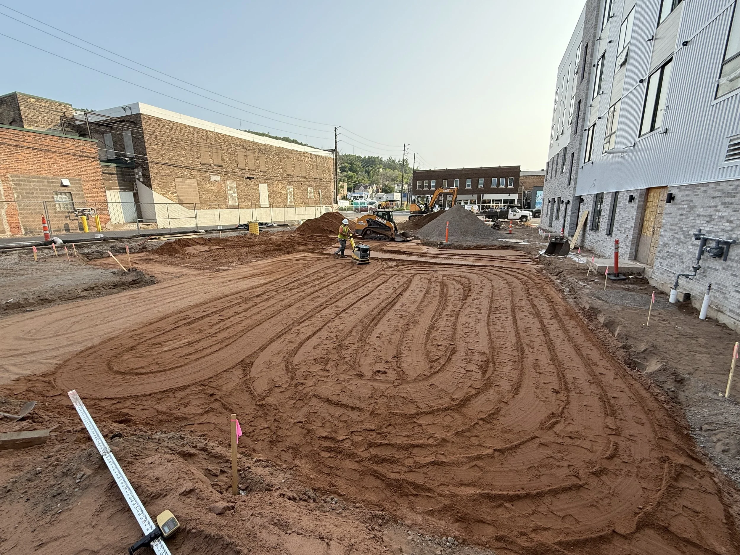 Construction site with cleared, leveled dirt, construction workers, and construction equipment in an urban area.