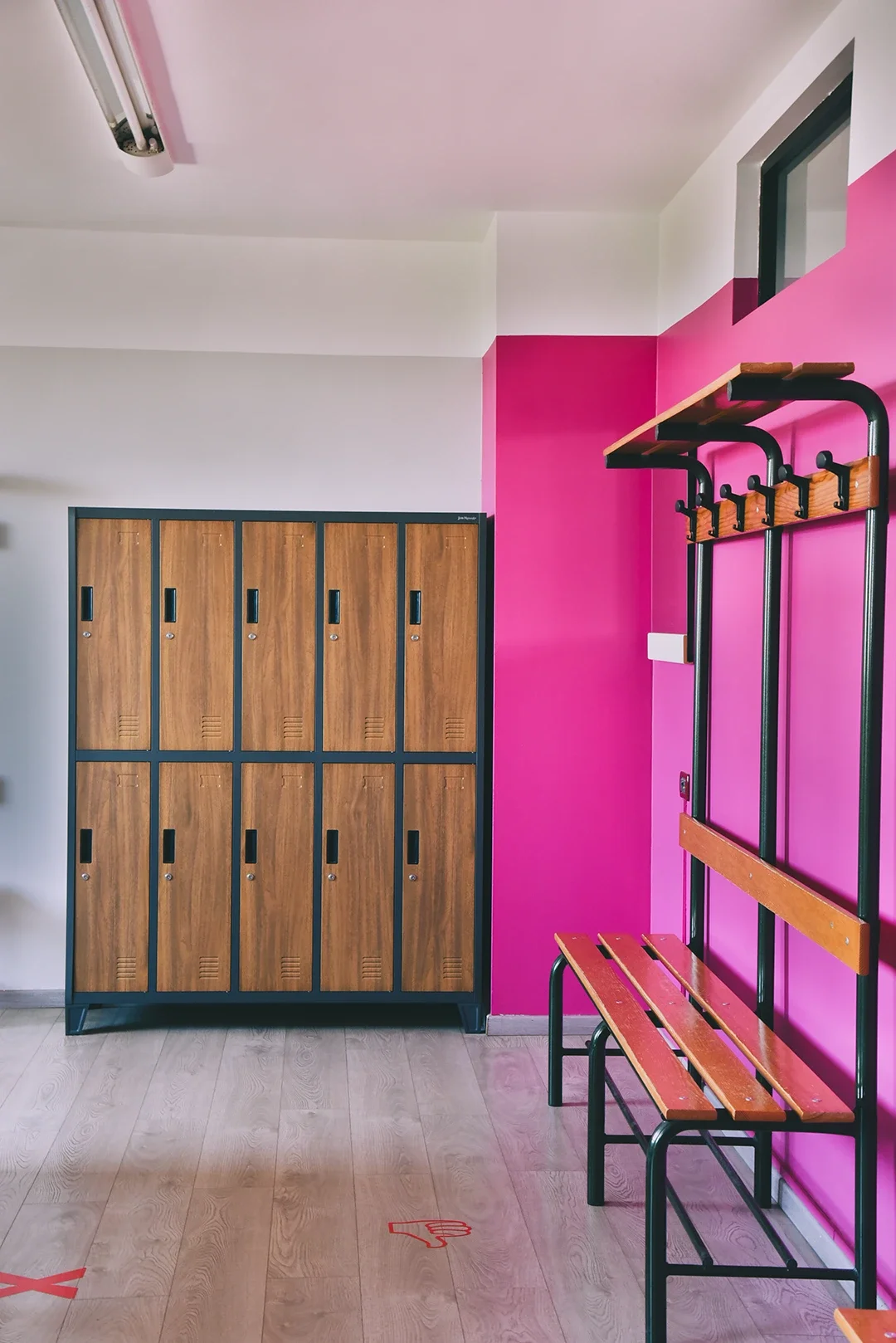Spogliatoio con armadietti di legno e panchine con ganci su parete rosa.
