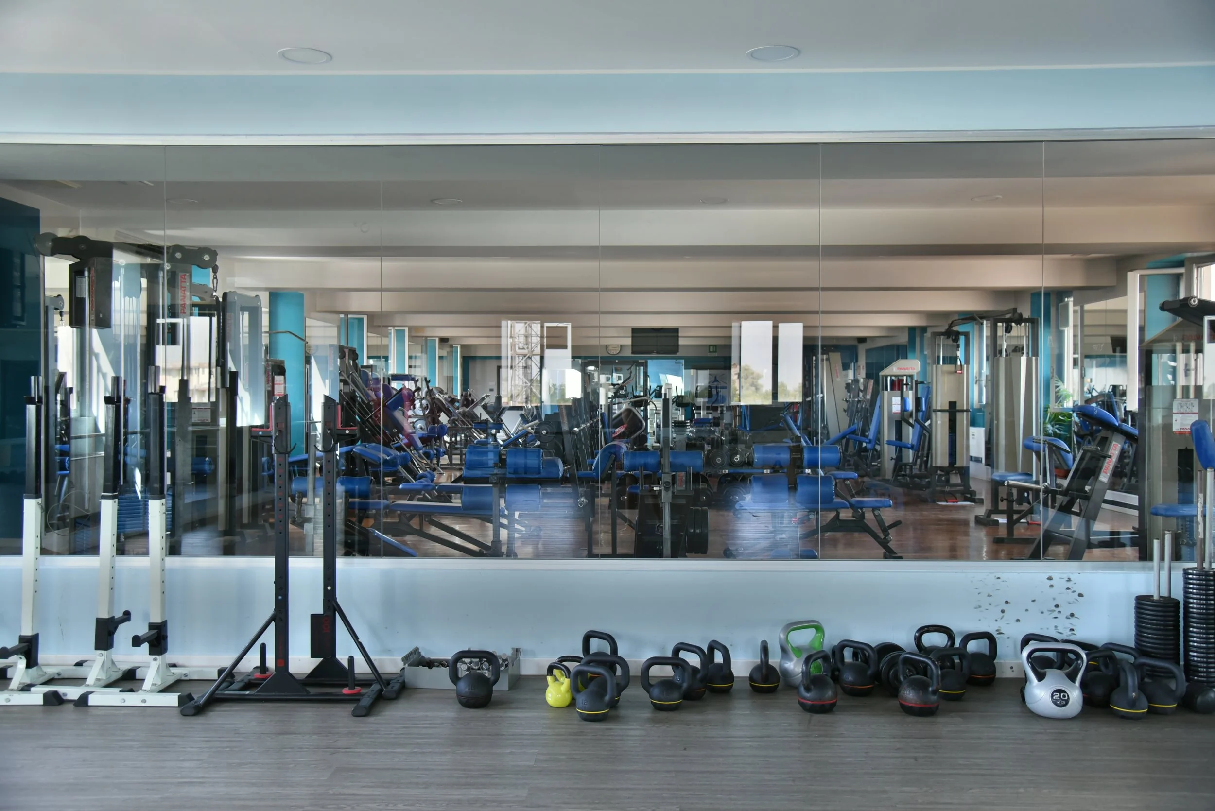 Palestra con attrezzature per esercizi, specchi alle pareti e kettlebell posizionati sul pavimento.