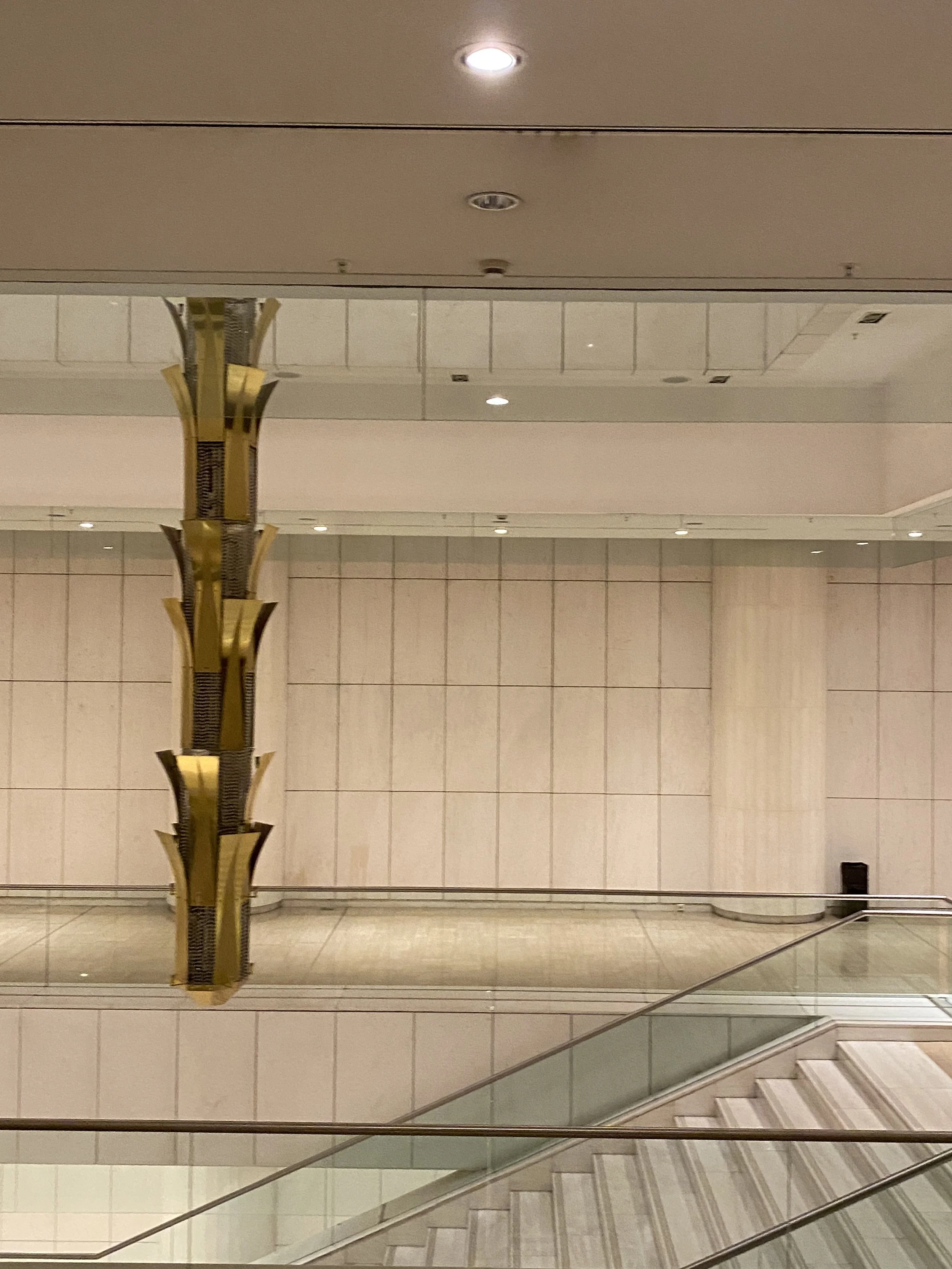 Empty interior of a modern building with a stairway, wall tiles, ceiling lights, and a decorative hanging element.
