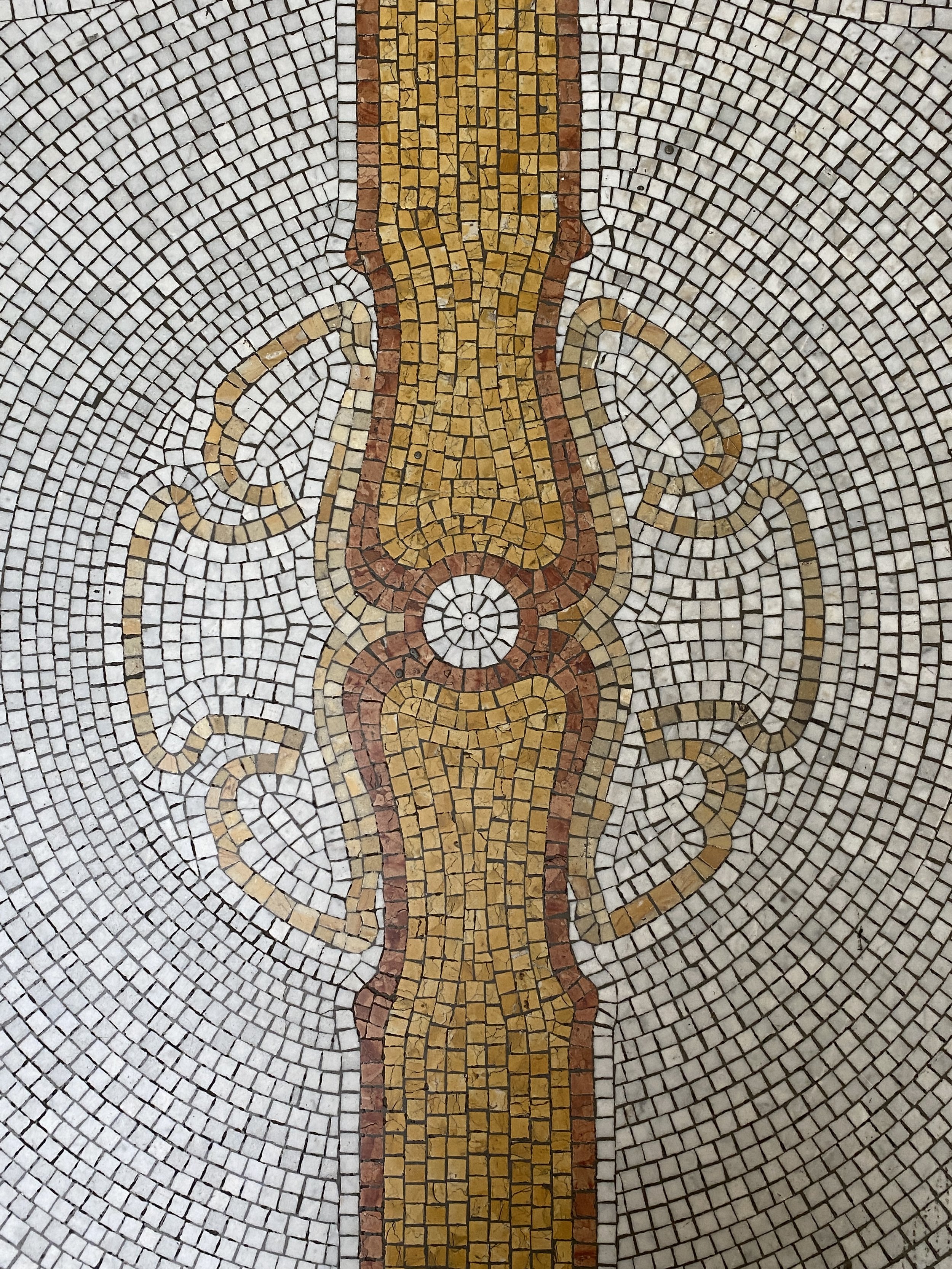 Colorful mosaic tile mural featuring a stylized torch or flame with swirling decorative elements on a concentric circle background.