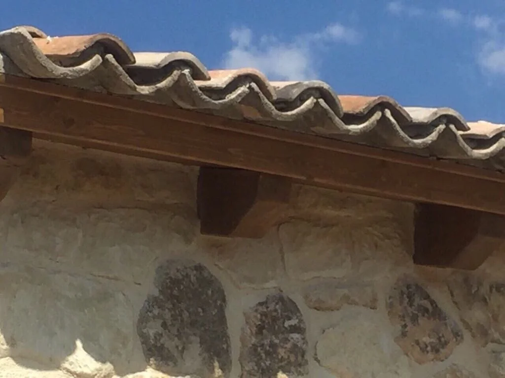 Close-up of a stone and wood building with clay-tiled roof and blue sky in background.