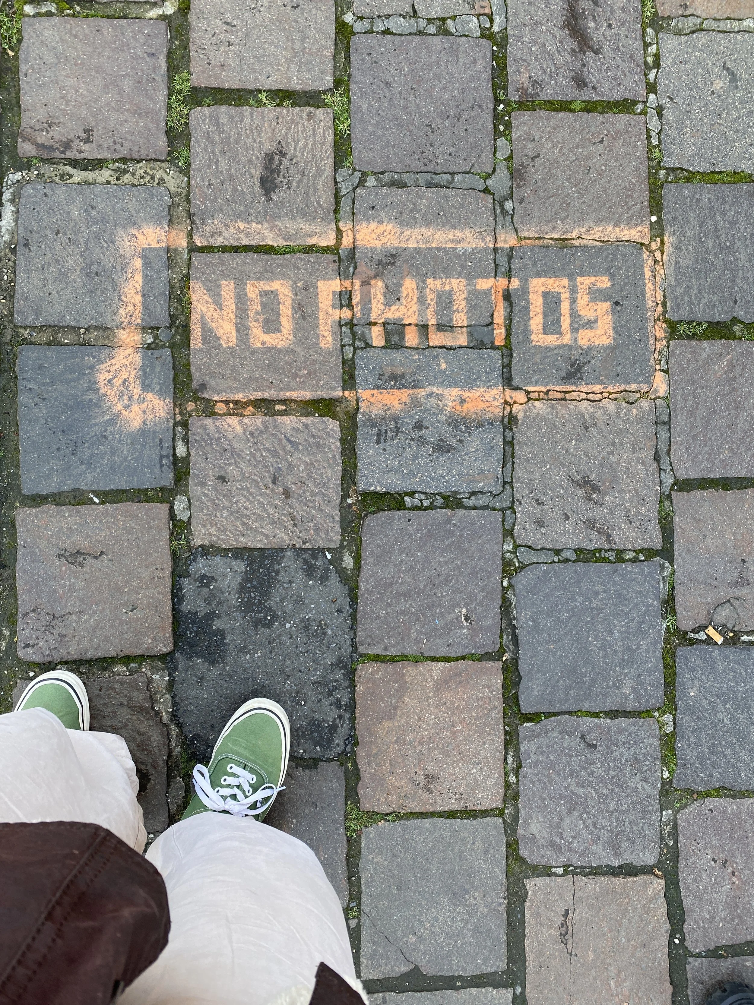 A cobblestone sidewalk with 'NO PHOTOS' spray-painted in orange on the stones.