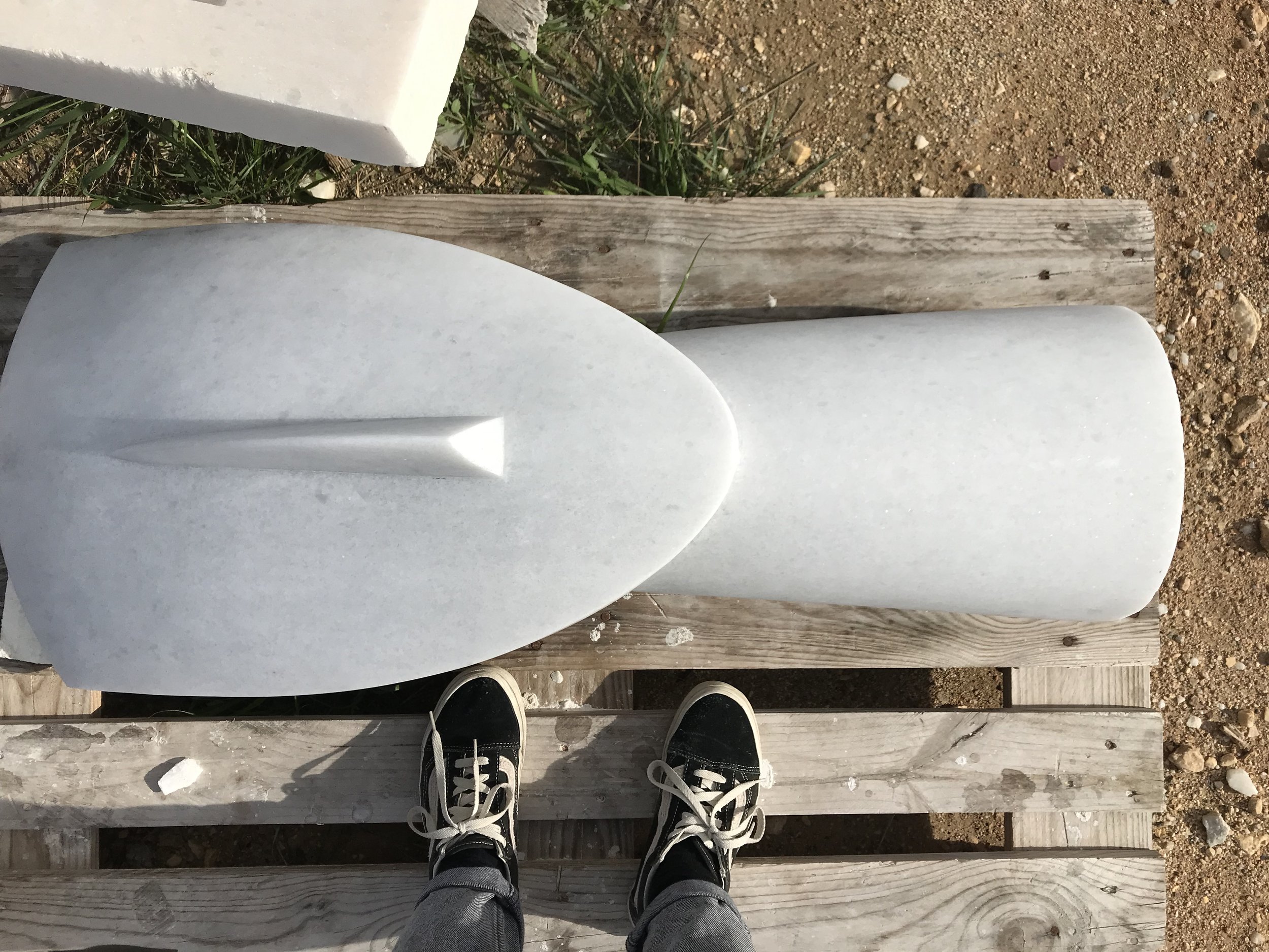 Photograph of a person's feet wearing black sneakers with white soles and laces, standing on a wooden pier or dock. The person is facing towards the water, and the photos are taken from a top-down perspective. The shoes are visible at the bottom of t
