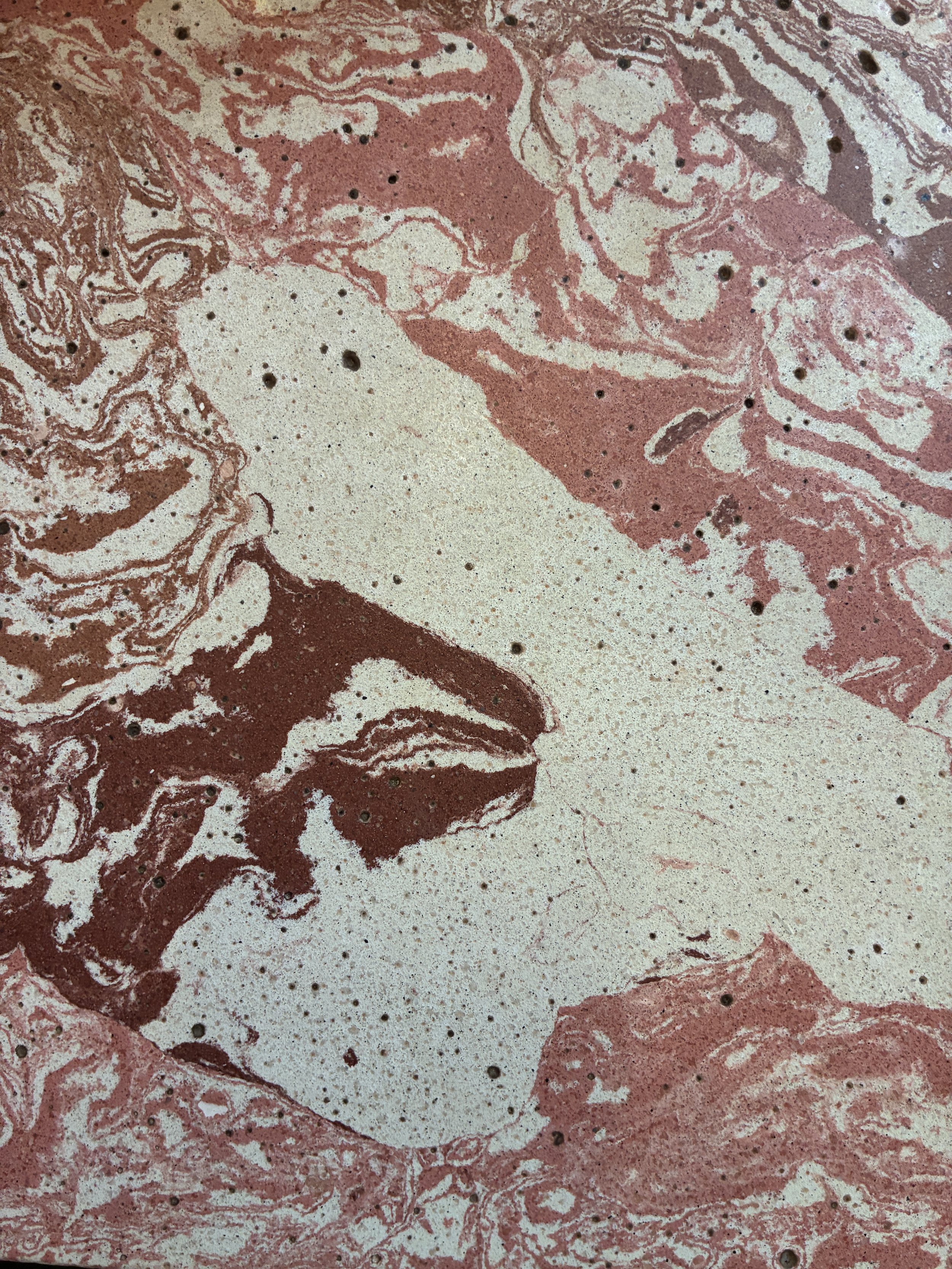Close-up of a marble surface with pink, white, and brown swirls and small black specks.