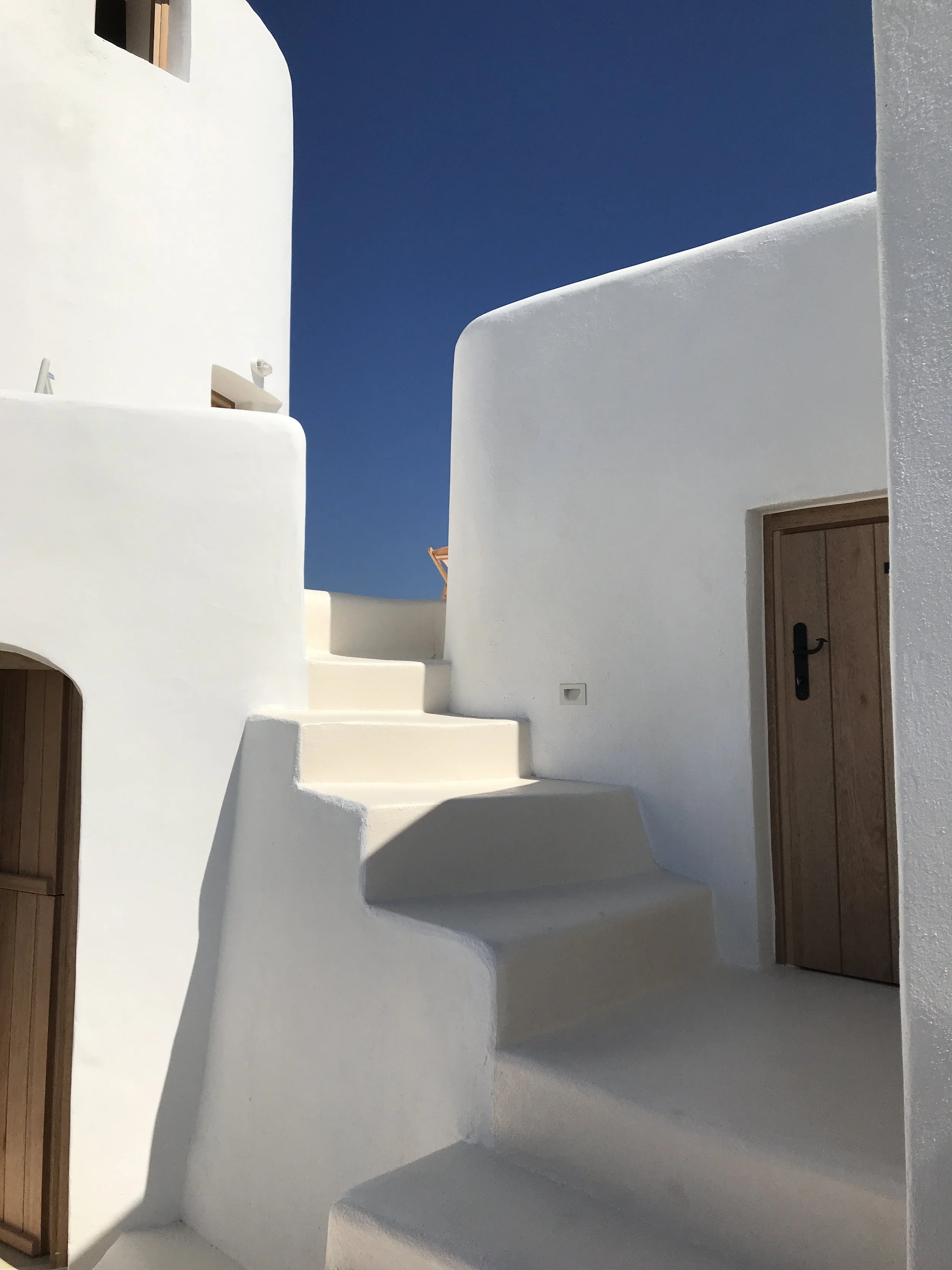 White stucco building with curved stairs and wooden doors, blue sky in the background.