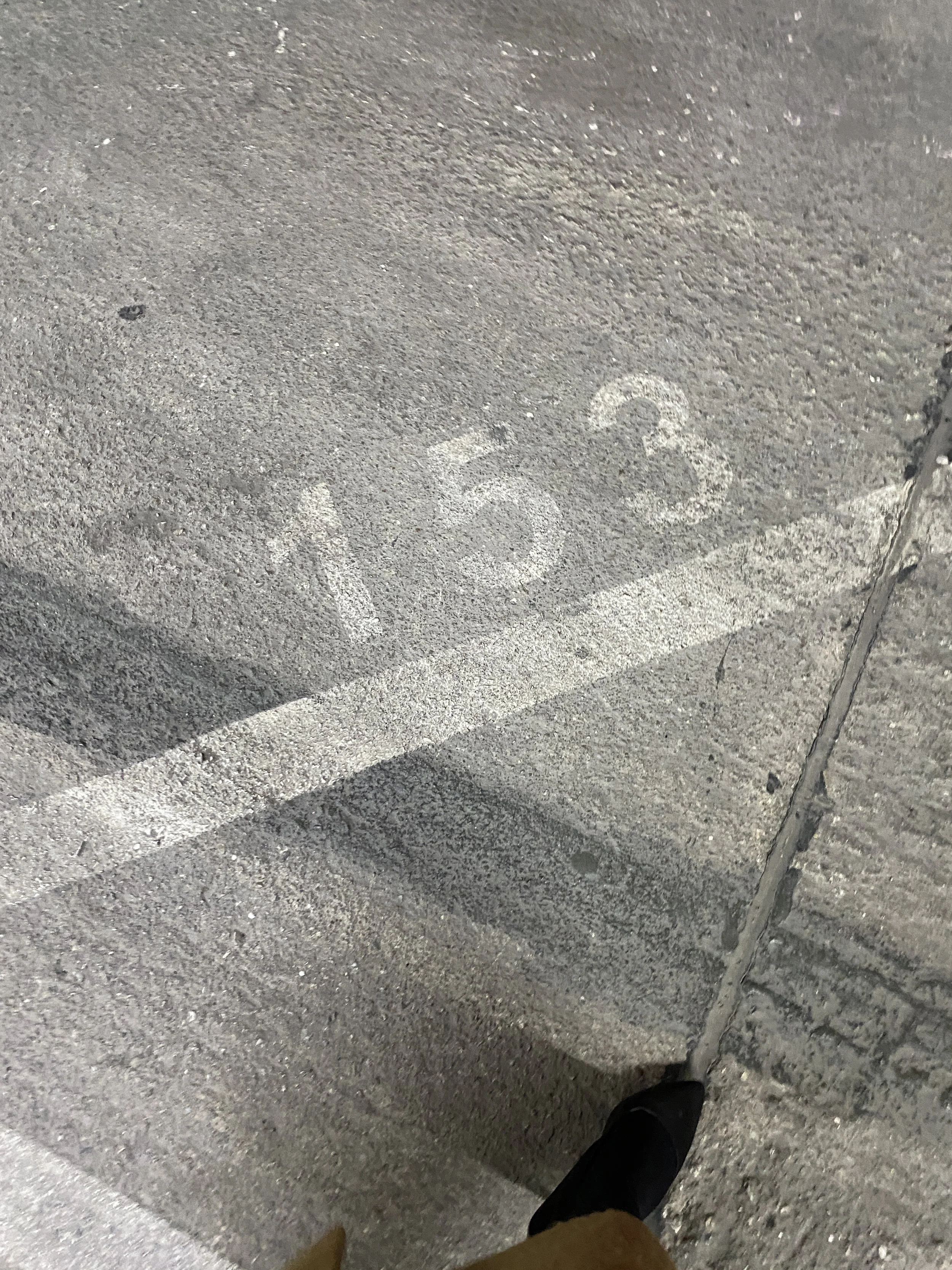 Numbered parking space 123 marked on asphalt ground near sidewalk with part of a shoe visible at bottom.