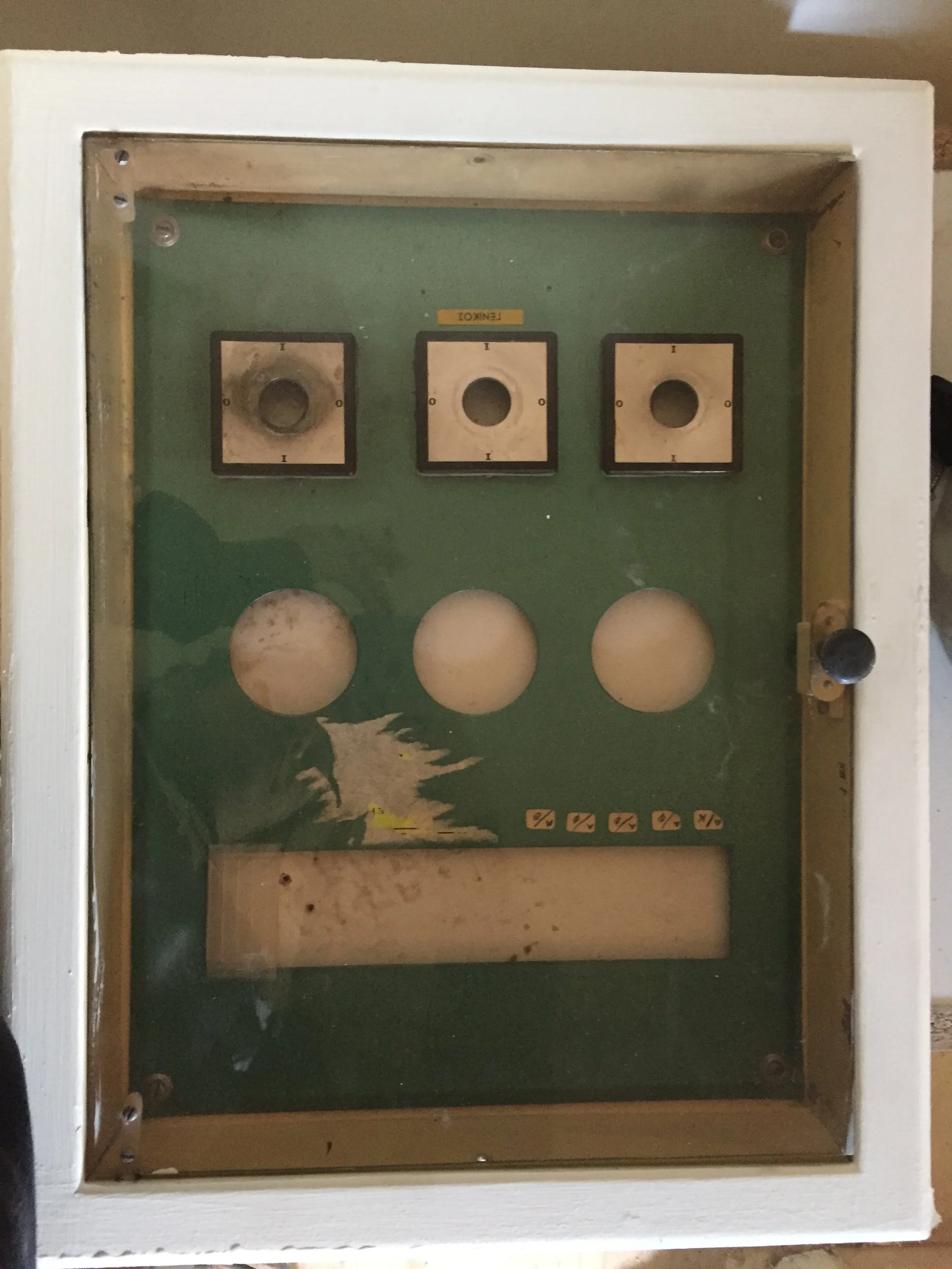 A vintage cigarette vending machine with a glass front, showing three empty compartments and a lower section with symbols and a slot for coins.