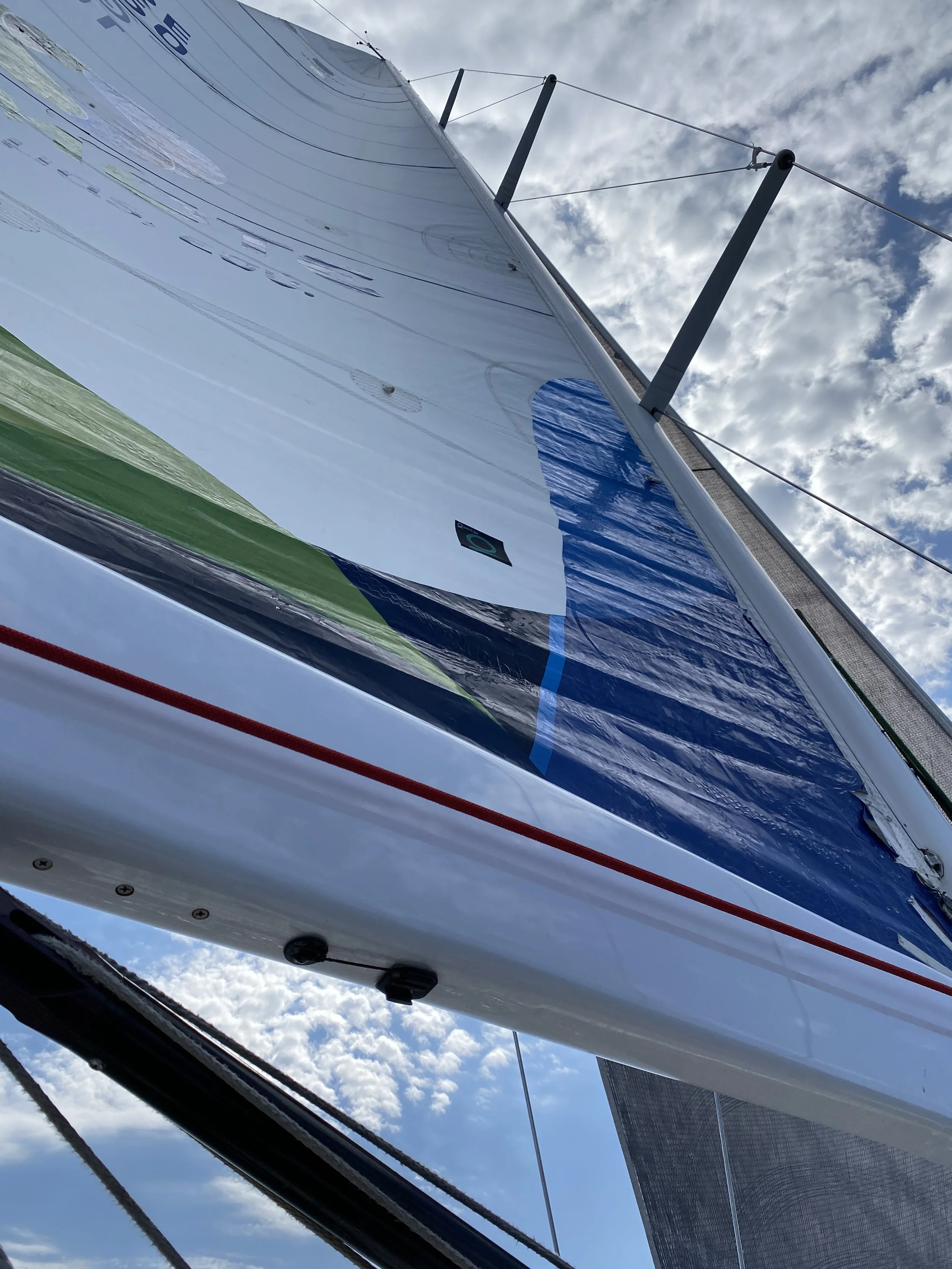 A sailboat viewed from below, highlighting the hull and sail against a partly cloudy sky.