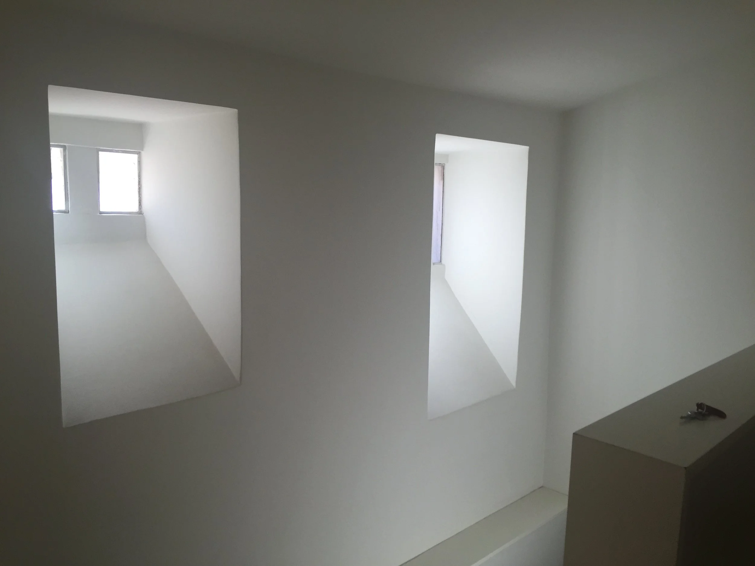 Empty white room with three rectangular openings in the wall, allowing natural light to enter. The room appears unfinished or newly constructed.