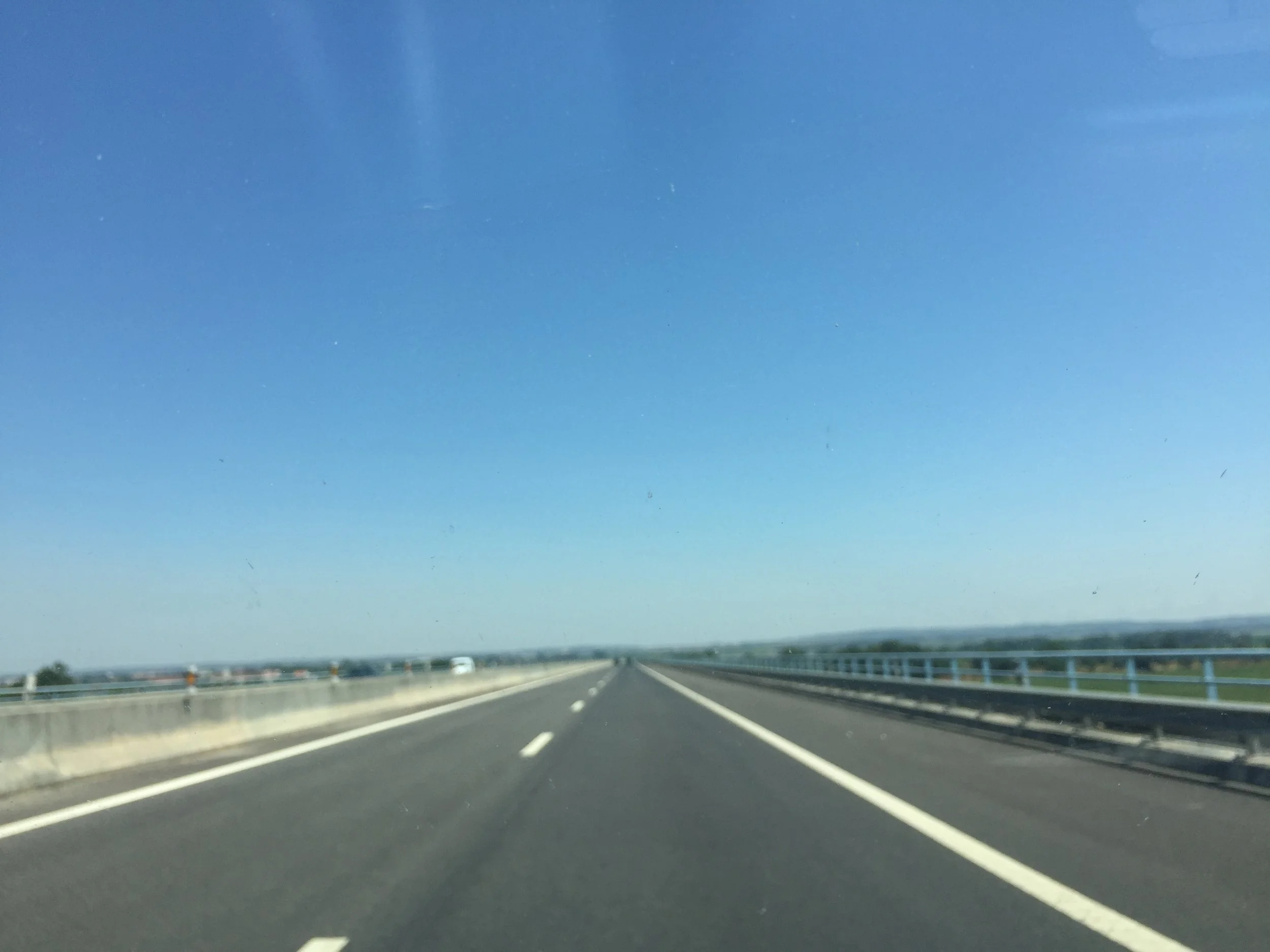 A view of a highway under a clear blue sky, with some distant trees and vehicles on the road.