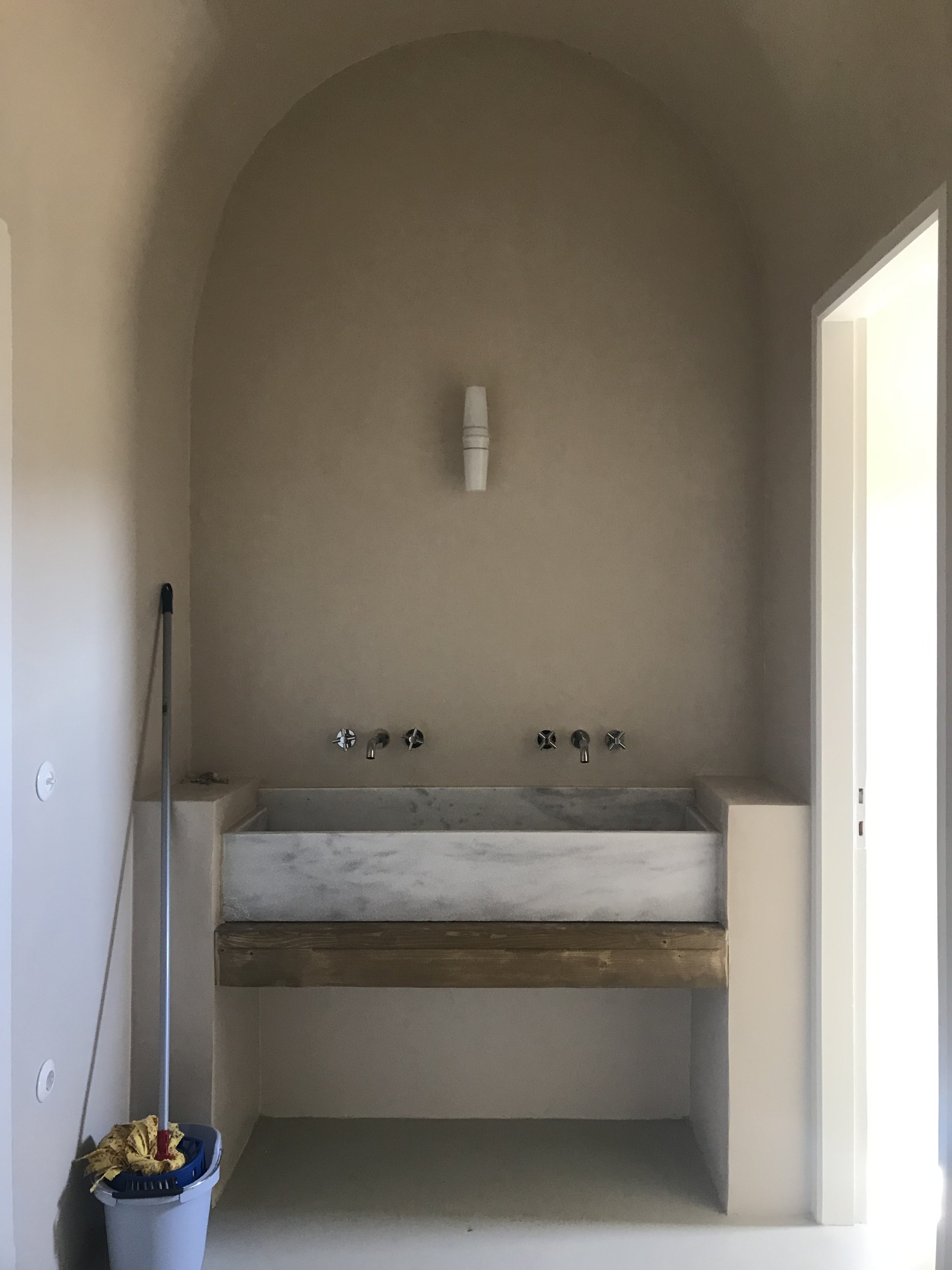 Empty laundry or utility room with a concrete sink, plumbing fixtures, and a mop leaning against the wall.