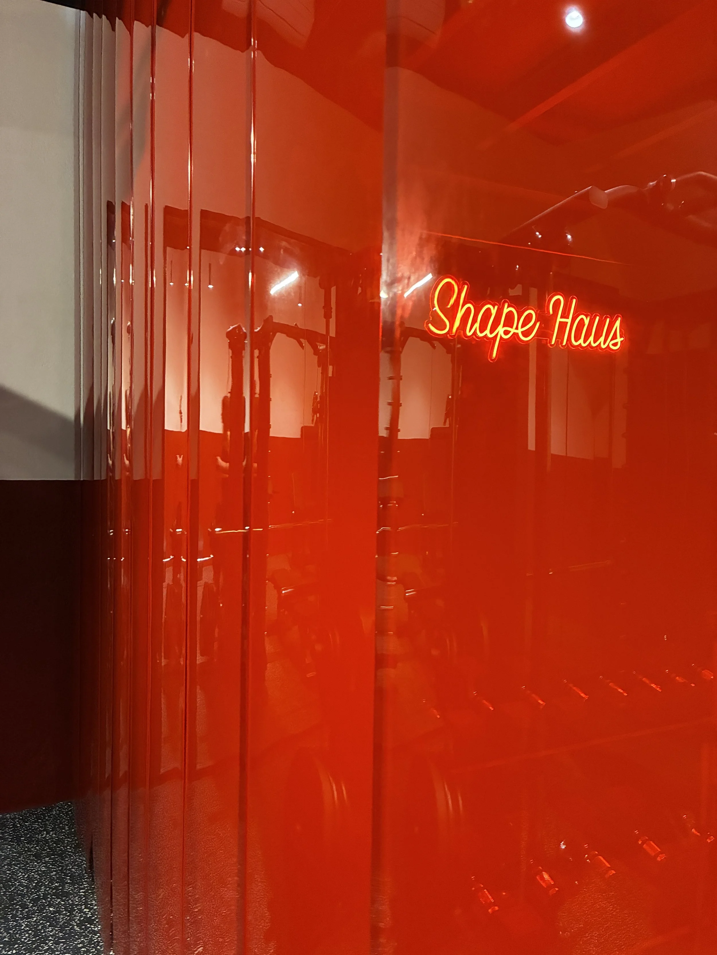 A red glass or plastic display case with a neon sign that reads 'Shape Haus' in red cursive letters.
