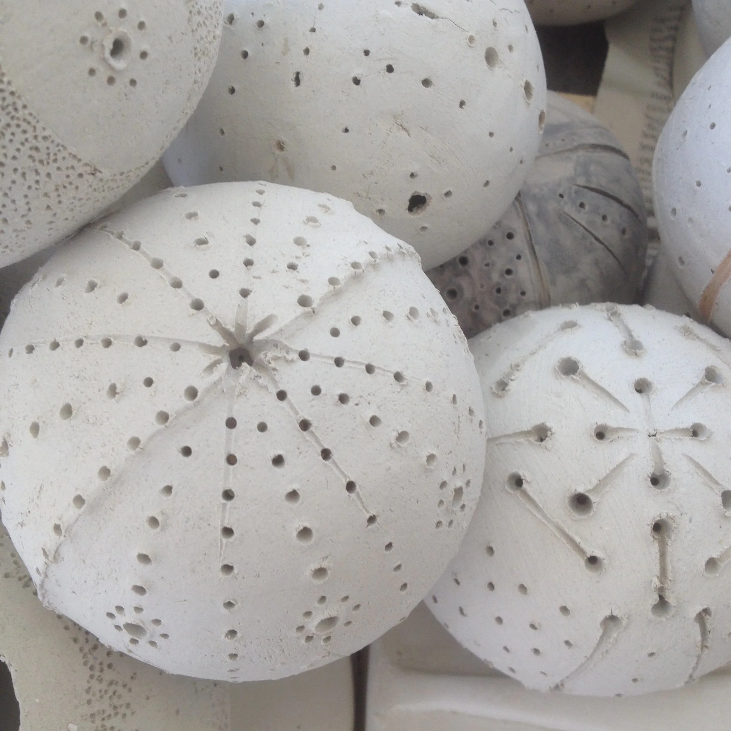 Close-up of multiple white, porous, ceramic spherical objects with numerous small holes.
