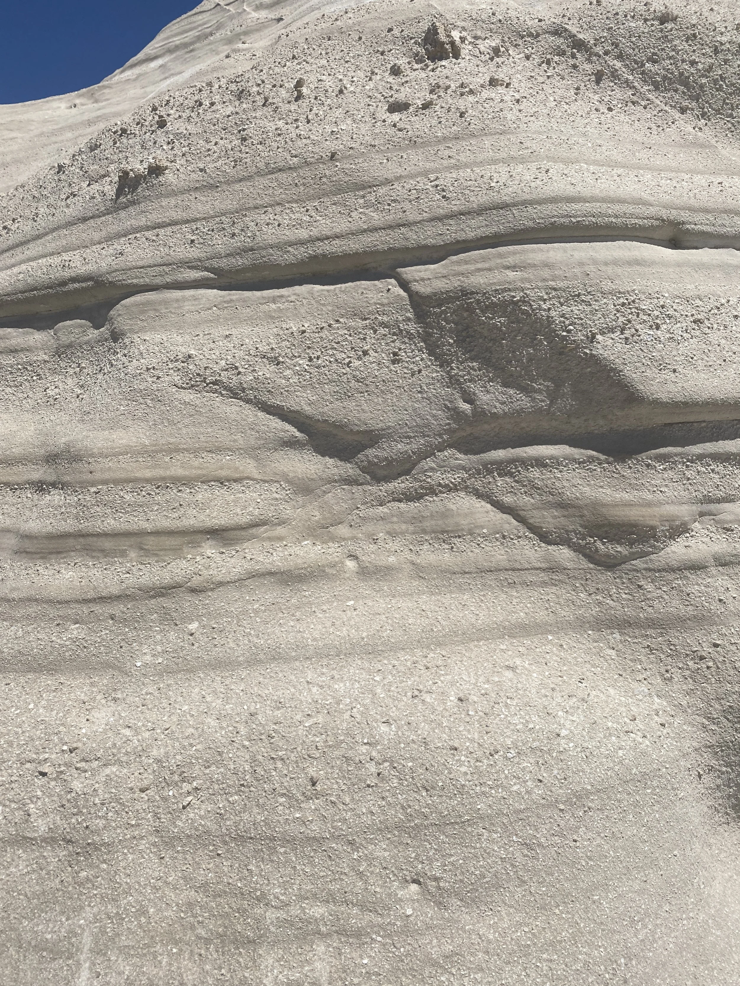 Close-up of layered sandstone rock formations with horizontal striations under a clear blue sky.
