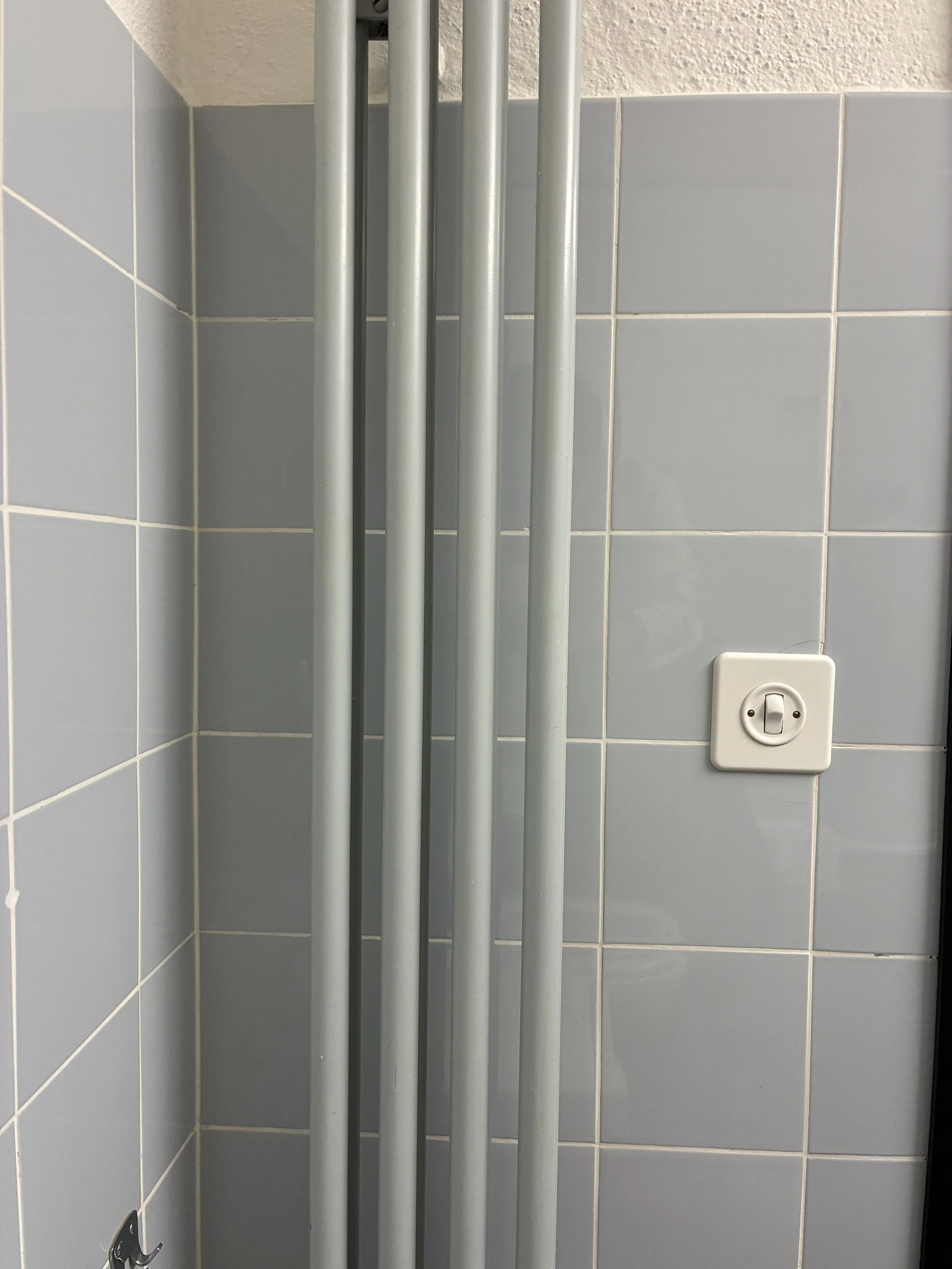 Four vertical metal pipes in a corner of a tiled wall with a white electrical outlet.