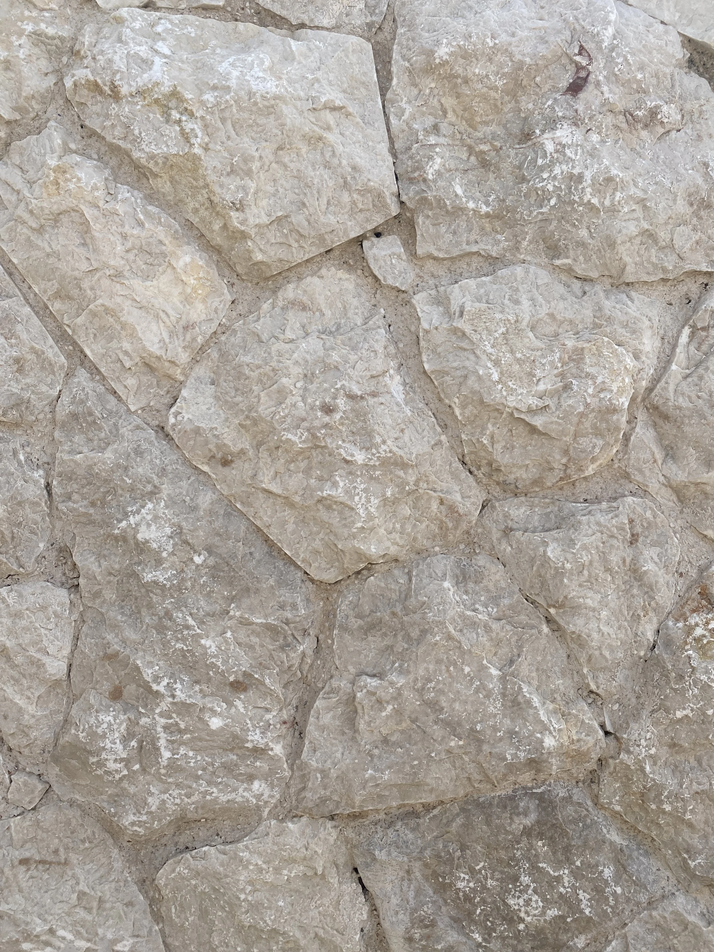 Close-up of a beige-colored stone wall with irregularly shaped stones fitted together.