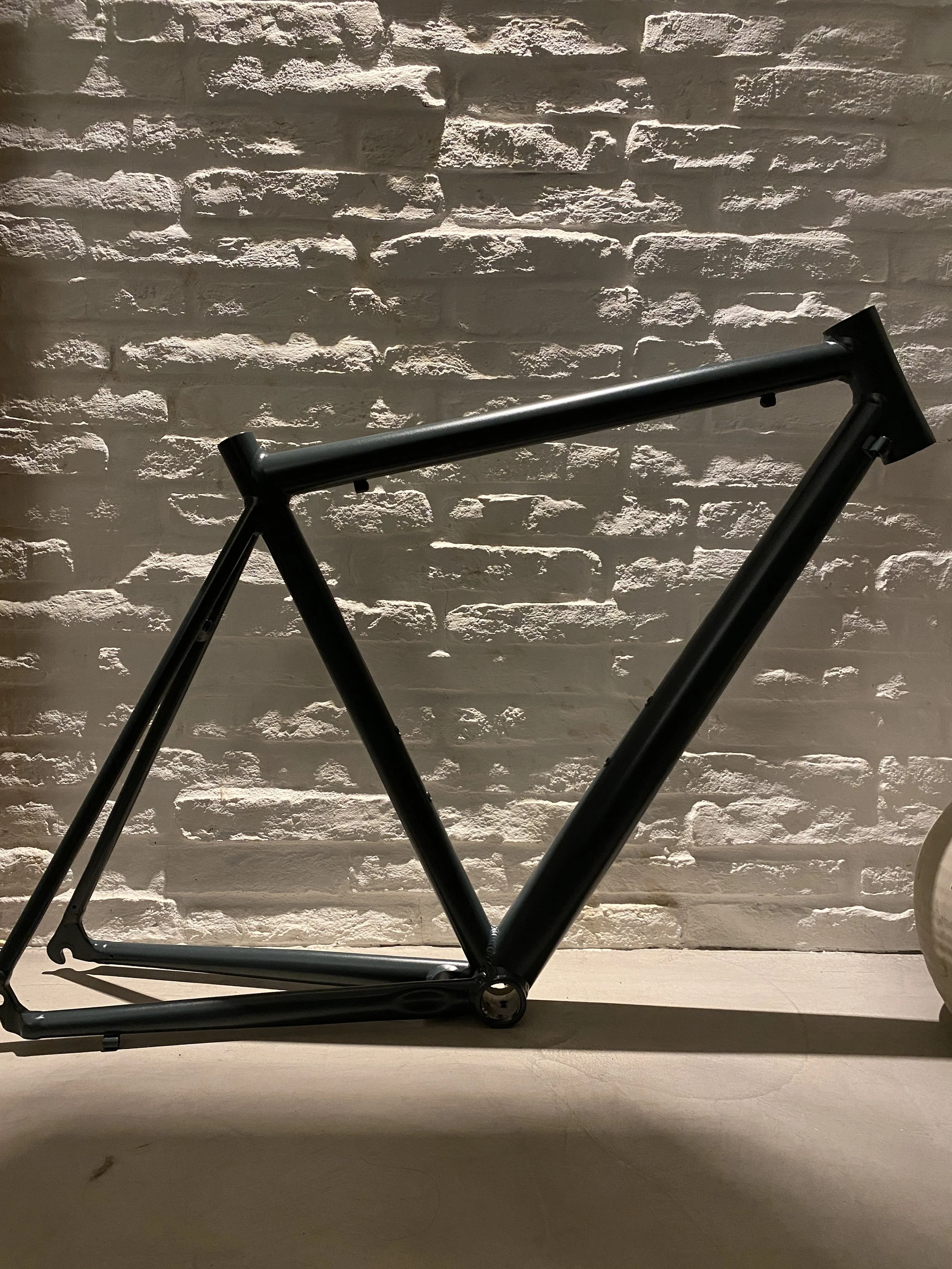 A black bicycle frame is leaning against a white brick wall with lighting casting shadows.