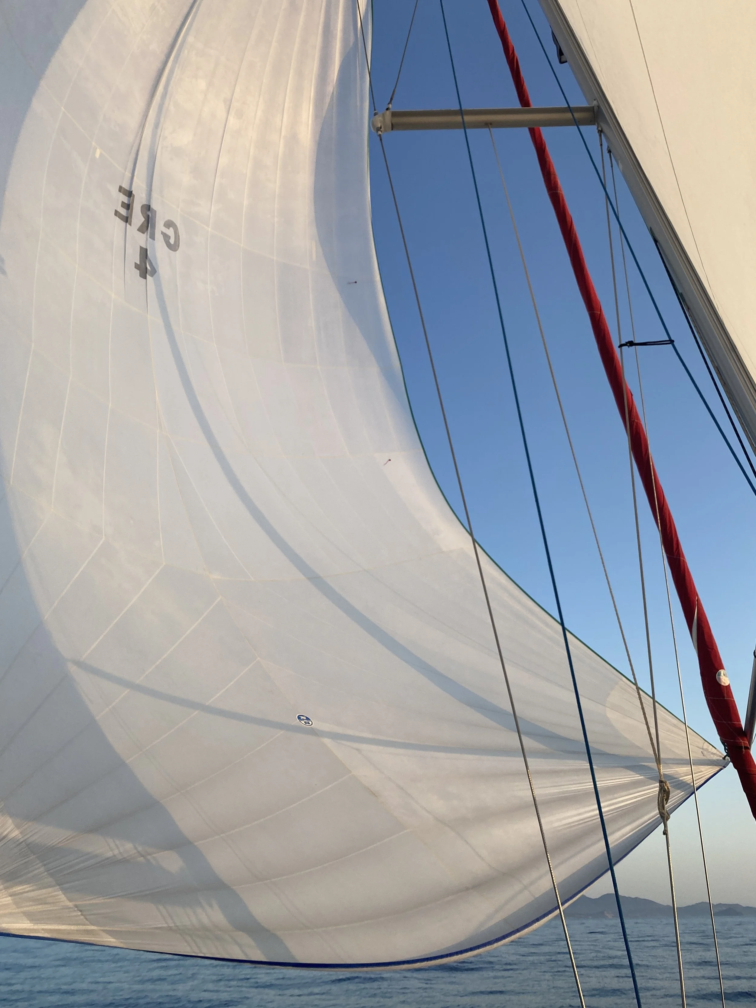 Close-up of sailing boat's white sail with blue sky and distant mountains in background