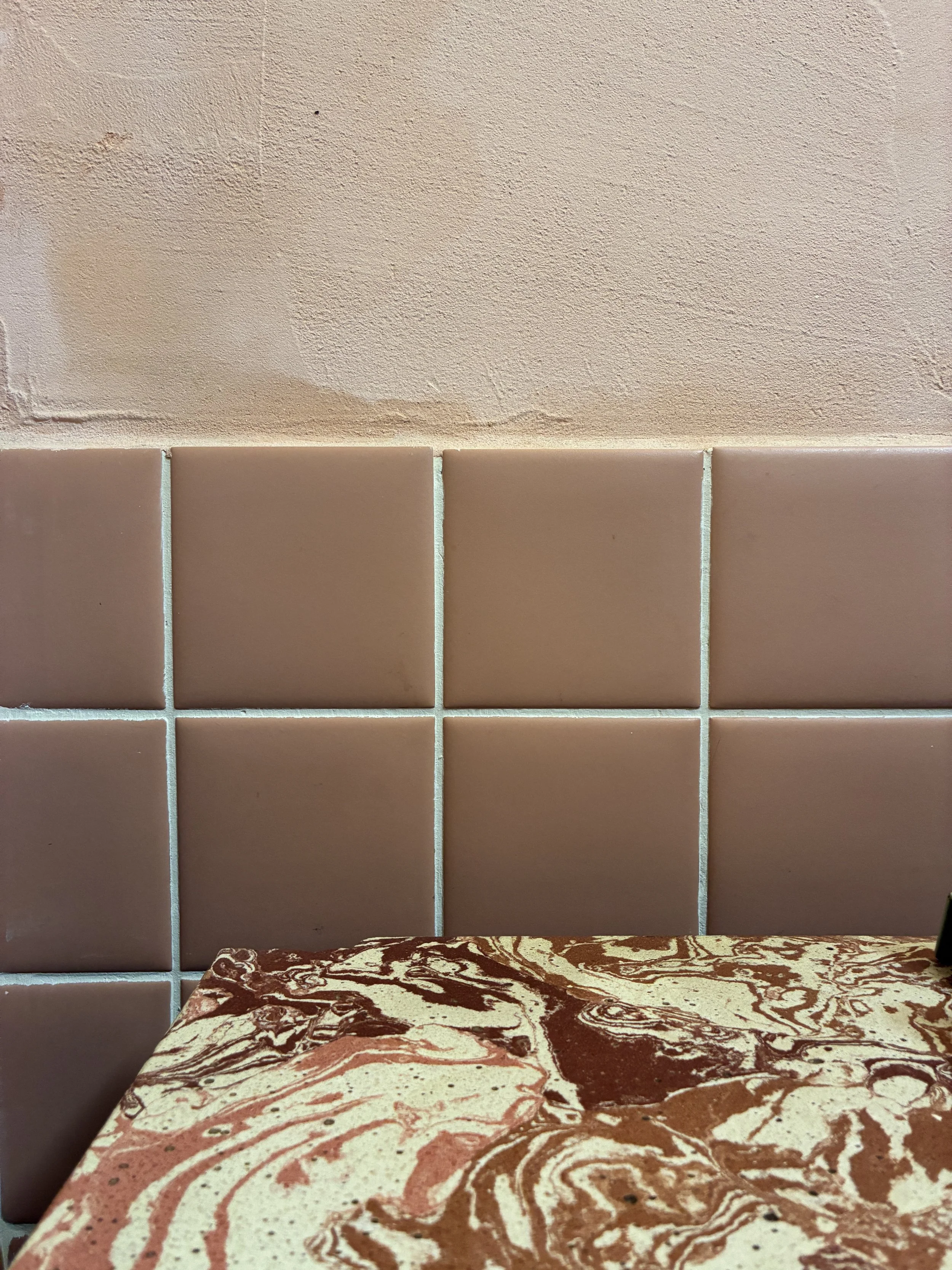 Interior scene showing a beige tiled wall with a textured beige wall above, and part of a marble-patterned table in the foreground.