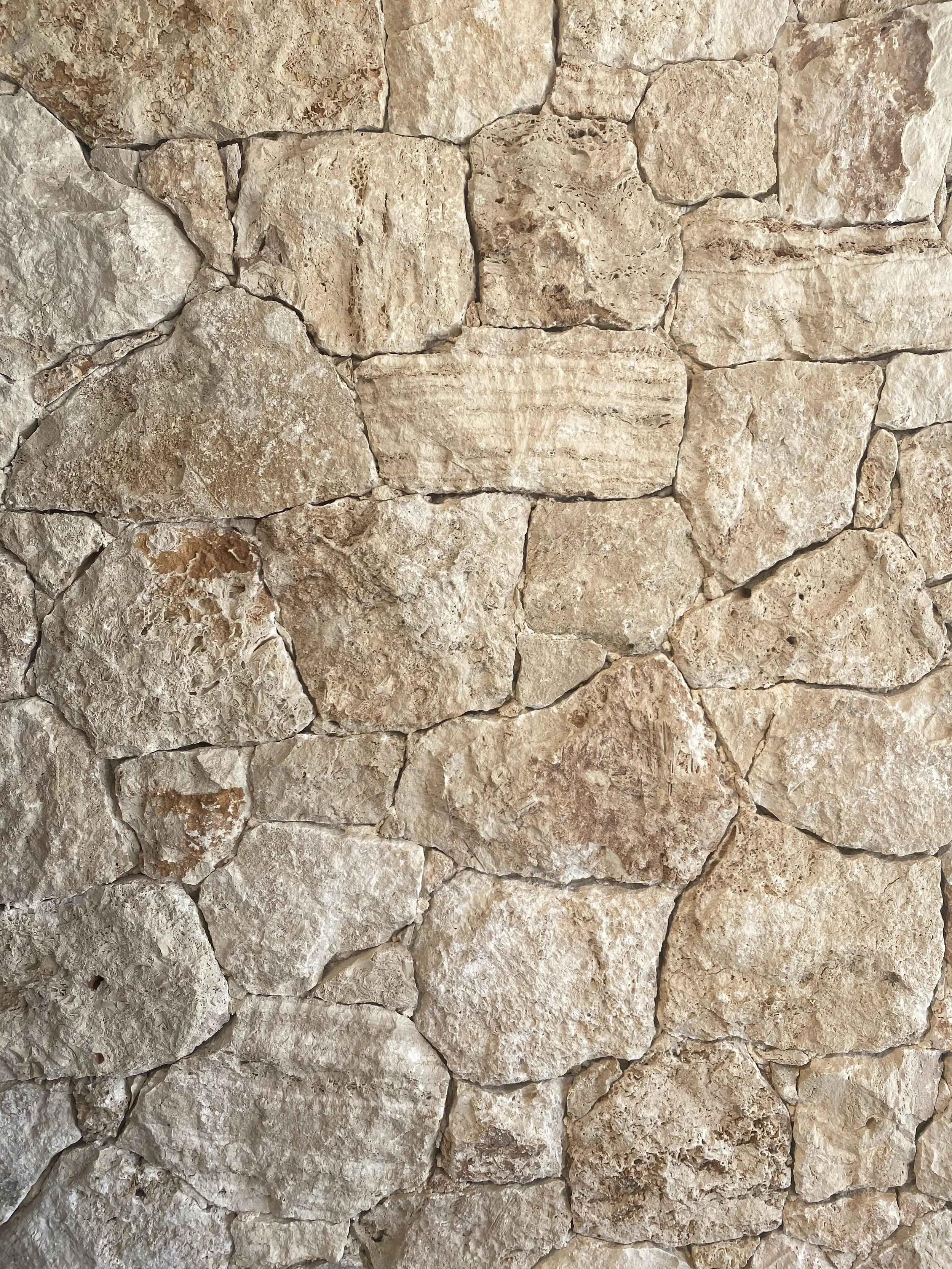 Close-up of a stone wall with irregularly shaped, beige and light brown stones fitted together.