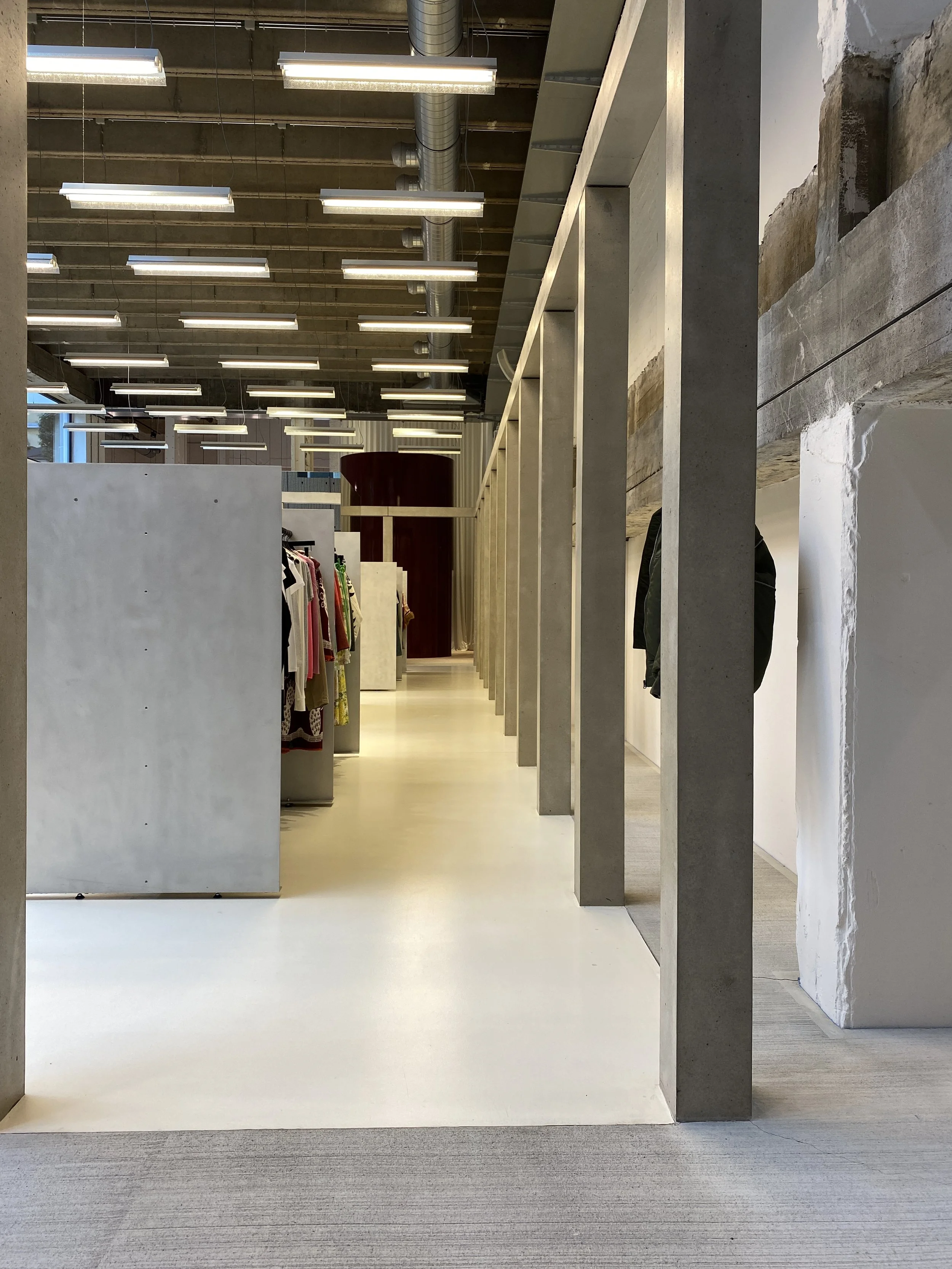 Modern clothing store interior with racks of clothes, minimalist design, and ceiling lights.