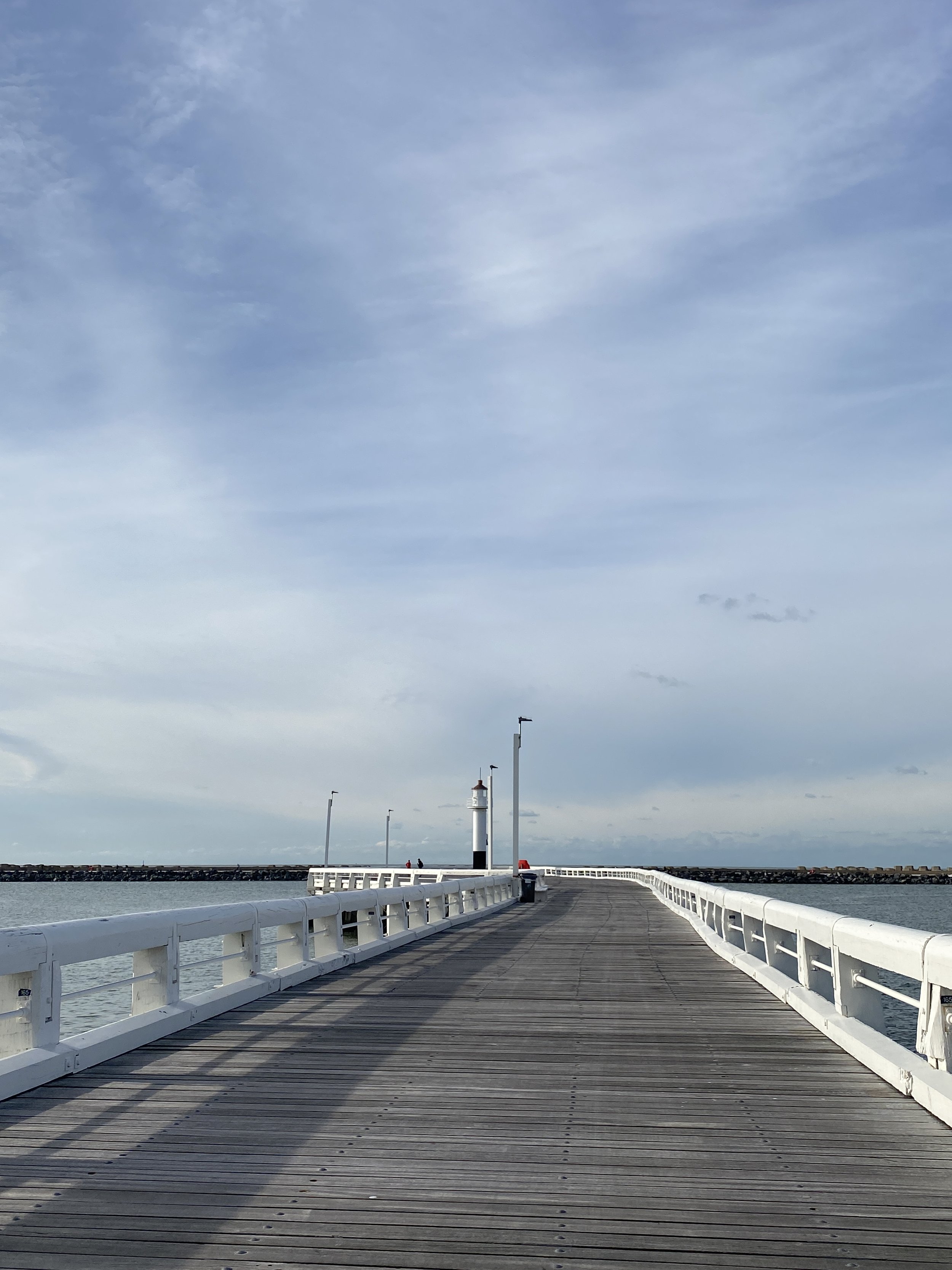 A wooden pier extending into the water with a small lighthouse at the end, surrounded by a partly cloudy sky.