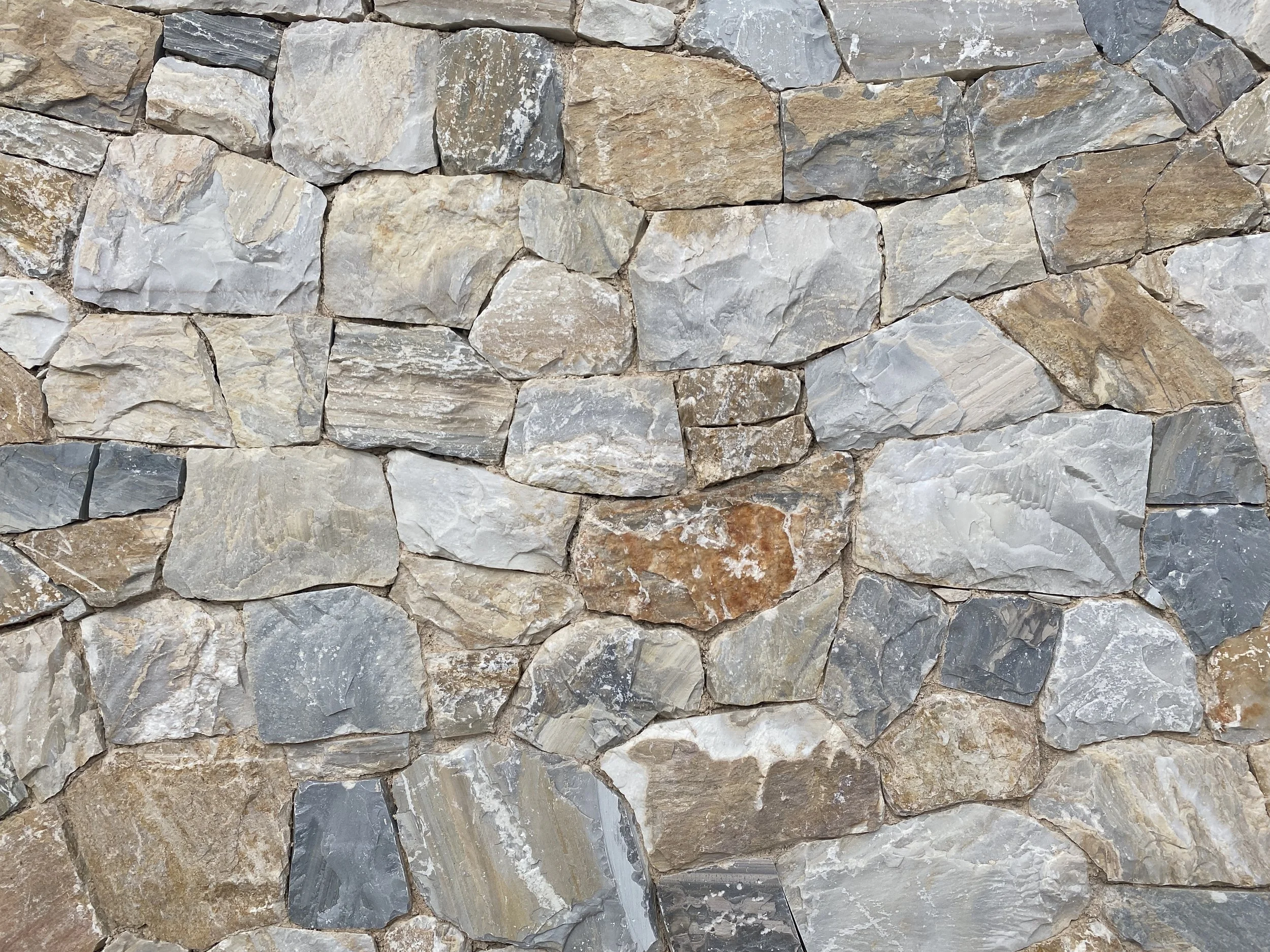 Close-up of a stone wall made of irregularly shaped grey and brown stones fitted together.