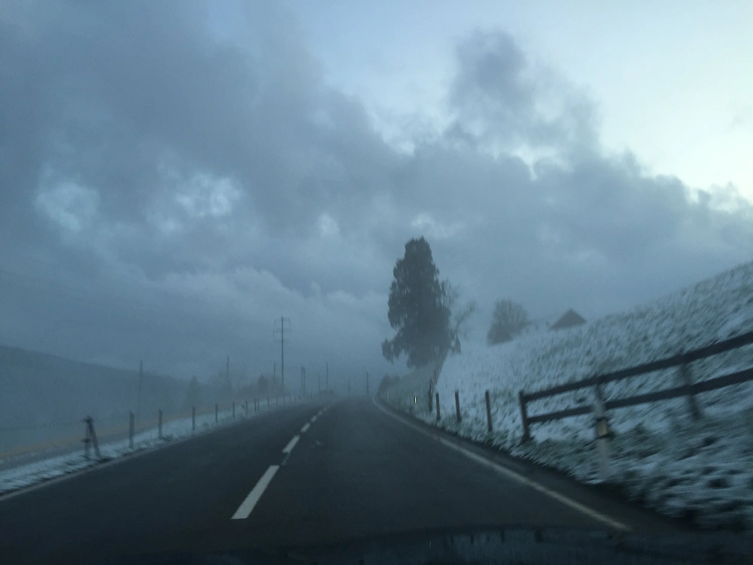 A dark, cloudy sky over a winding mountain road with guardrails and distance markers.