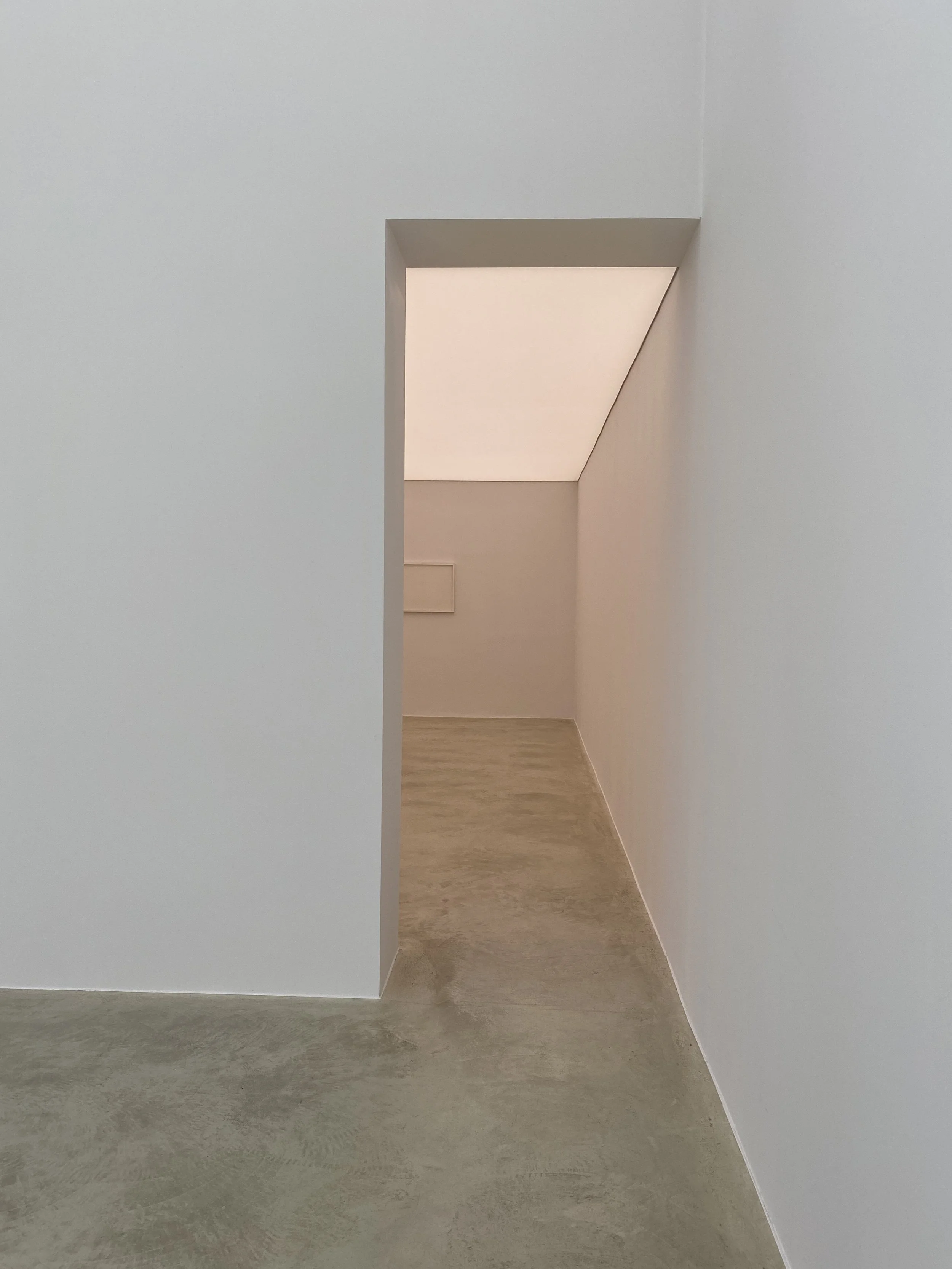 Minimalist interior space with white walls, a narrow entrance, and a sloped ceiling in the hallway.