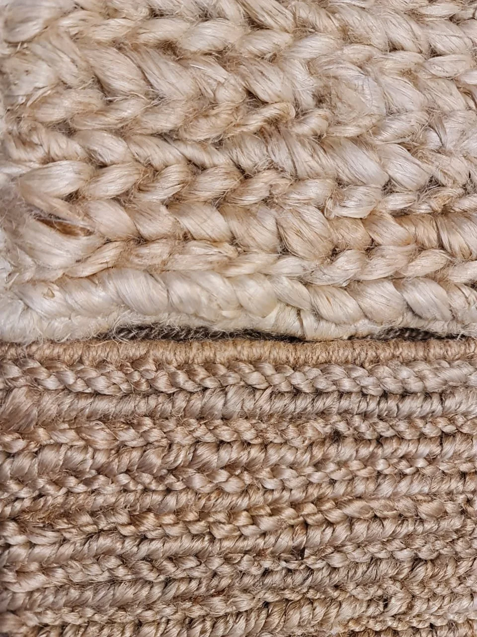 Close-up of two woven textured rugs, one above the other, made of thick, natural-colored fibers.