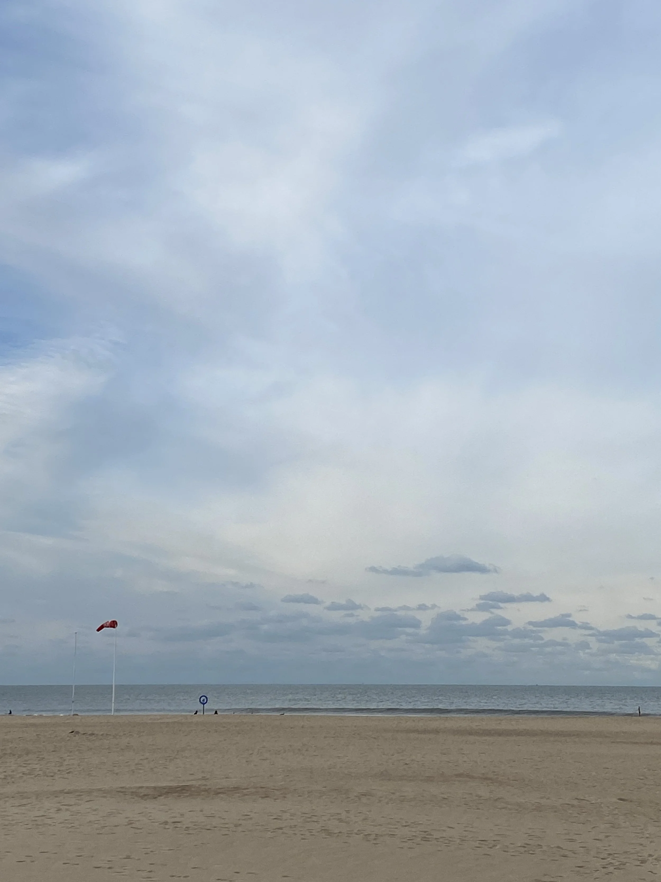 Empty beach with a red flag, cloudy sky, and calm ocean.