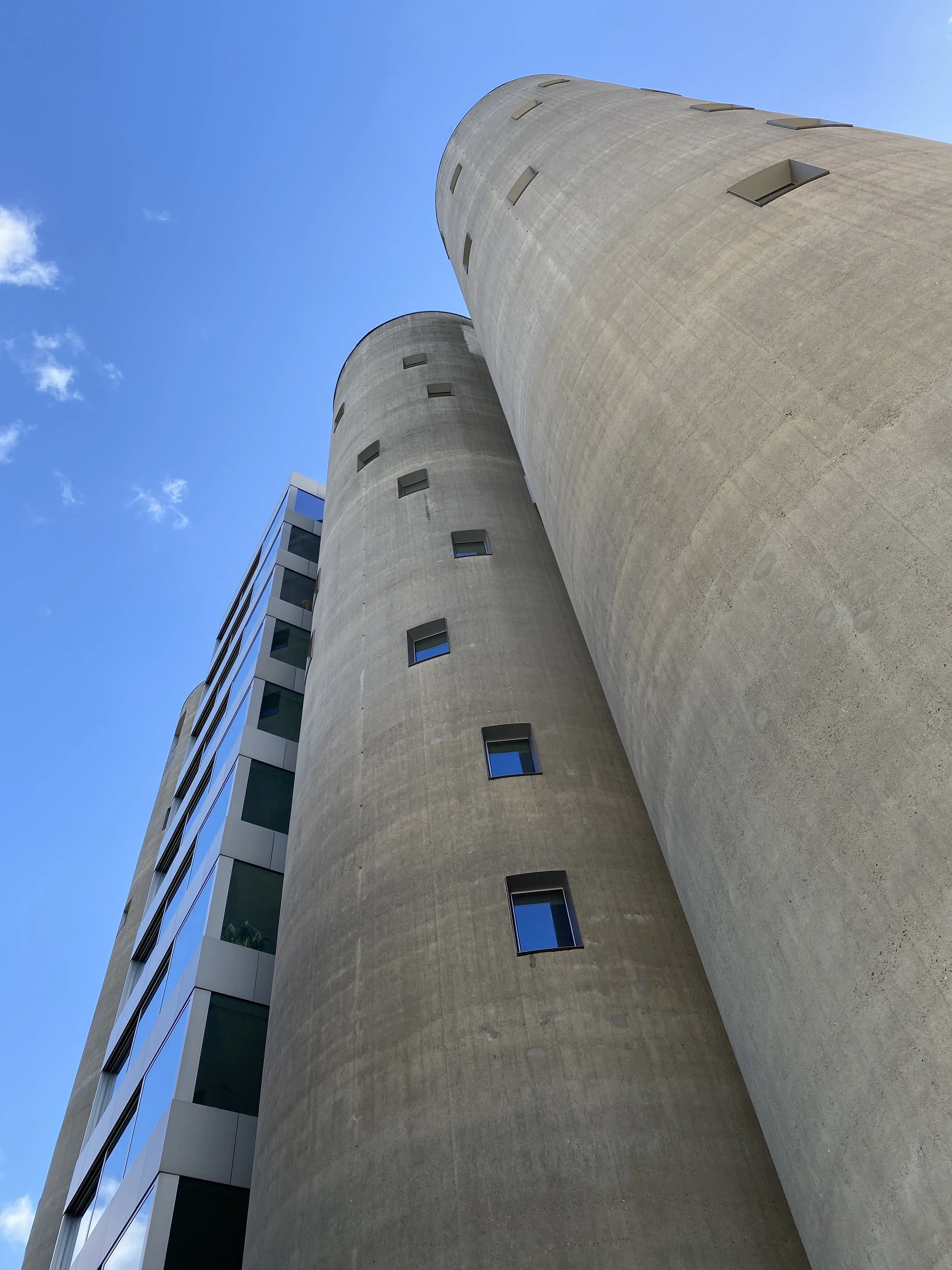Low-angle view of two tall concrete cylindrical buildings against a blue sky with a few clouds, showing windows and architectural details.