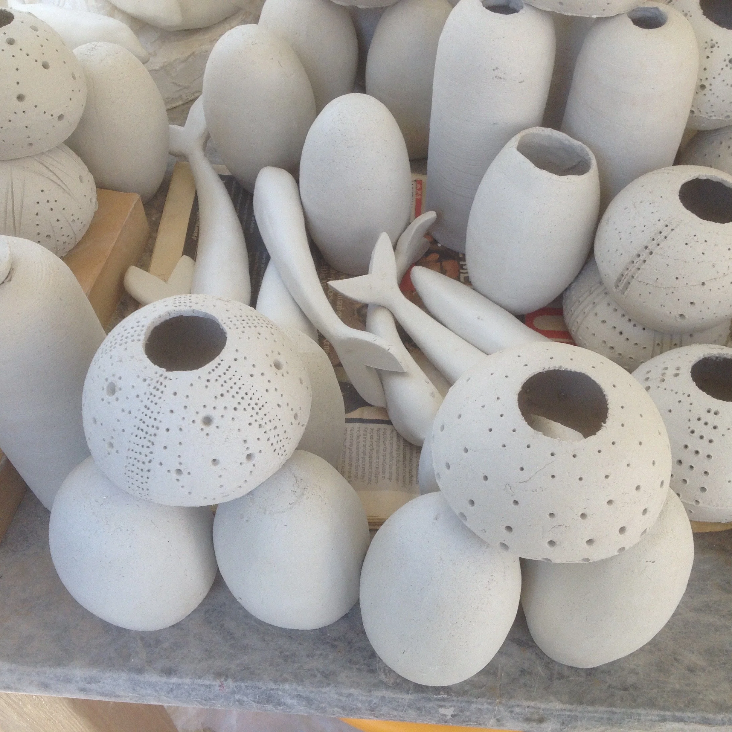 Collection of unfinished white ceramic vases and decorative objects, some with holes or textures, arranged on a surface.