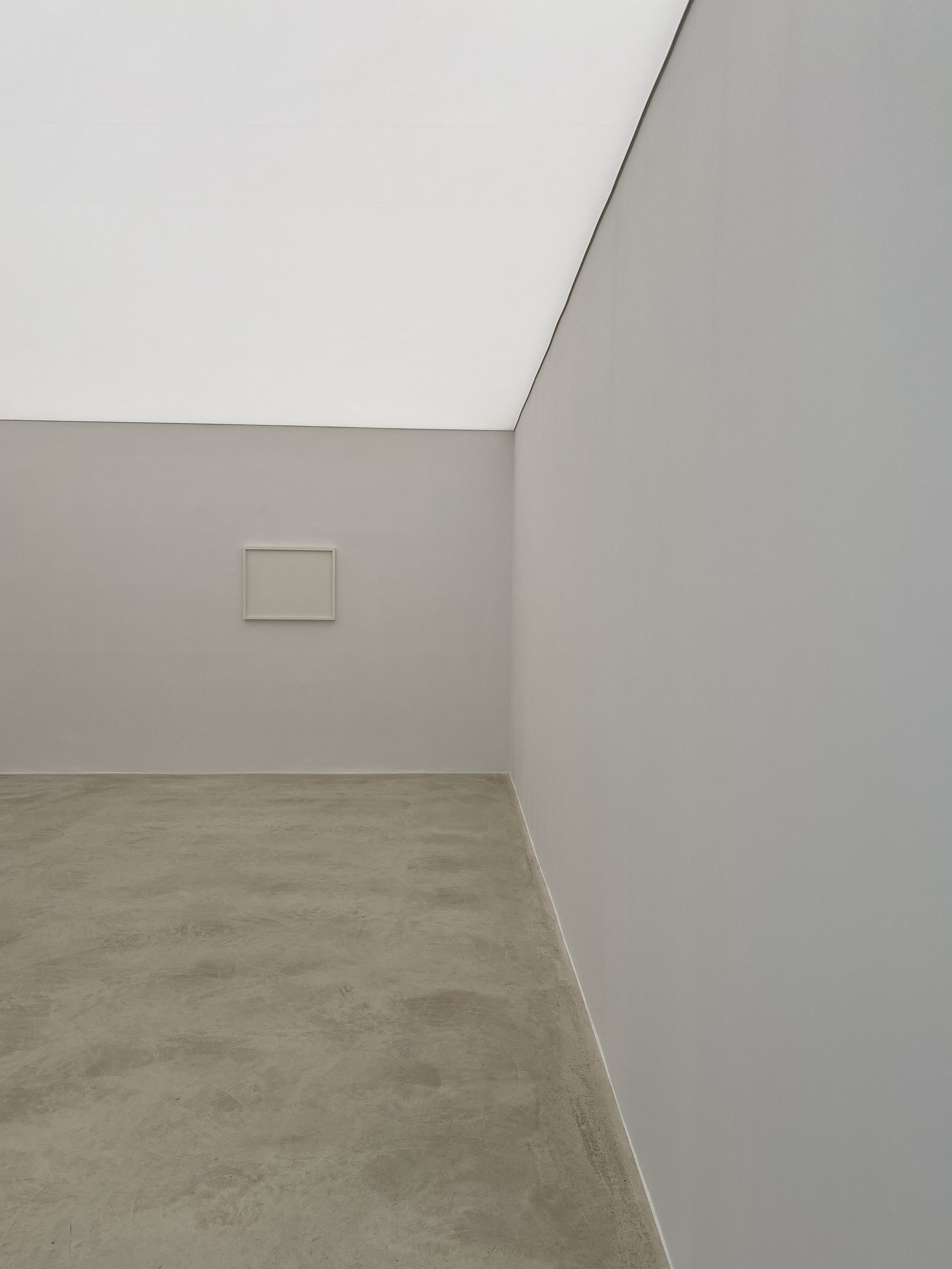Empty room with white and grey walls, a sloped ceiling, a vent on the wall, and a concrete floor.