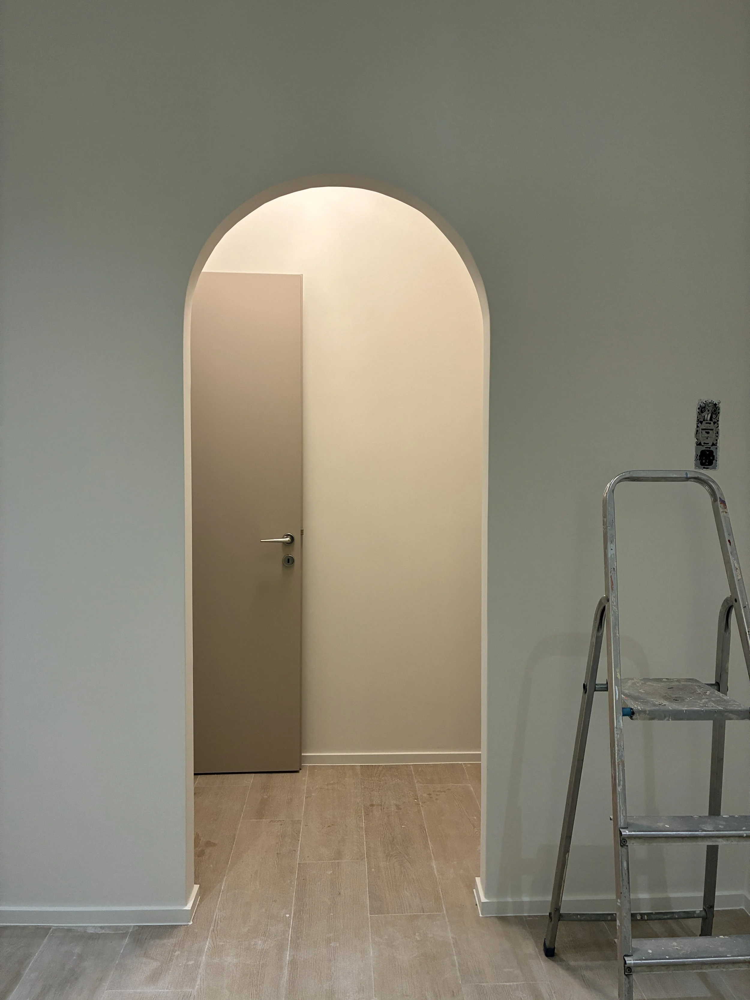 Interior view of a room with an arched doorway, a closed door inside, and a stepladder on the right side nearby.