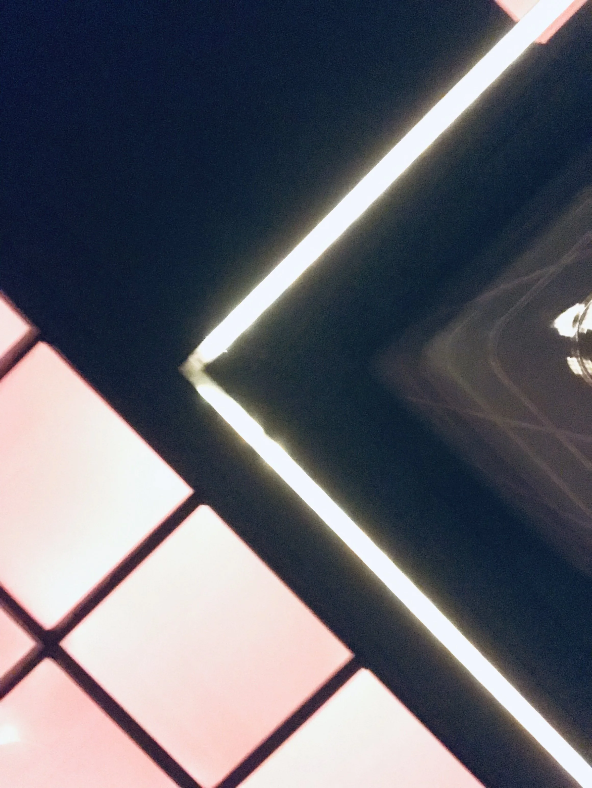 Close-up of a laptop keyboard with pink keys and black borders, with a black device and a white light strip in the background.