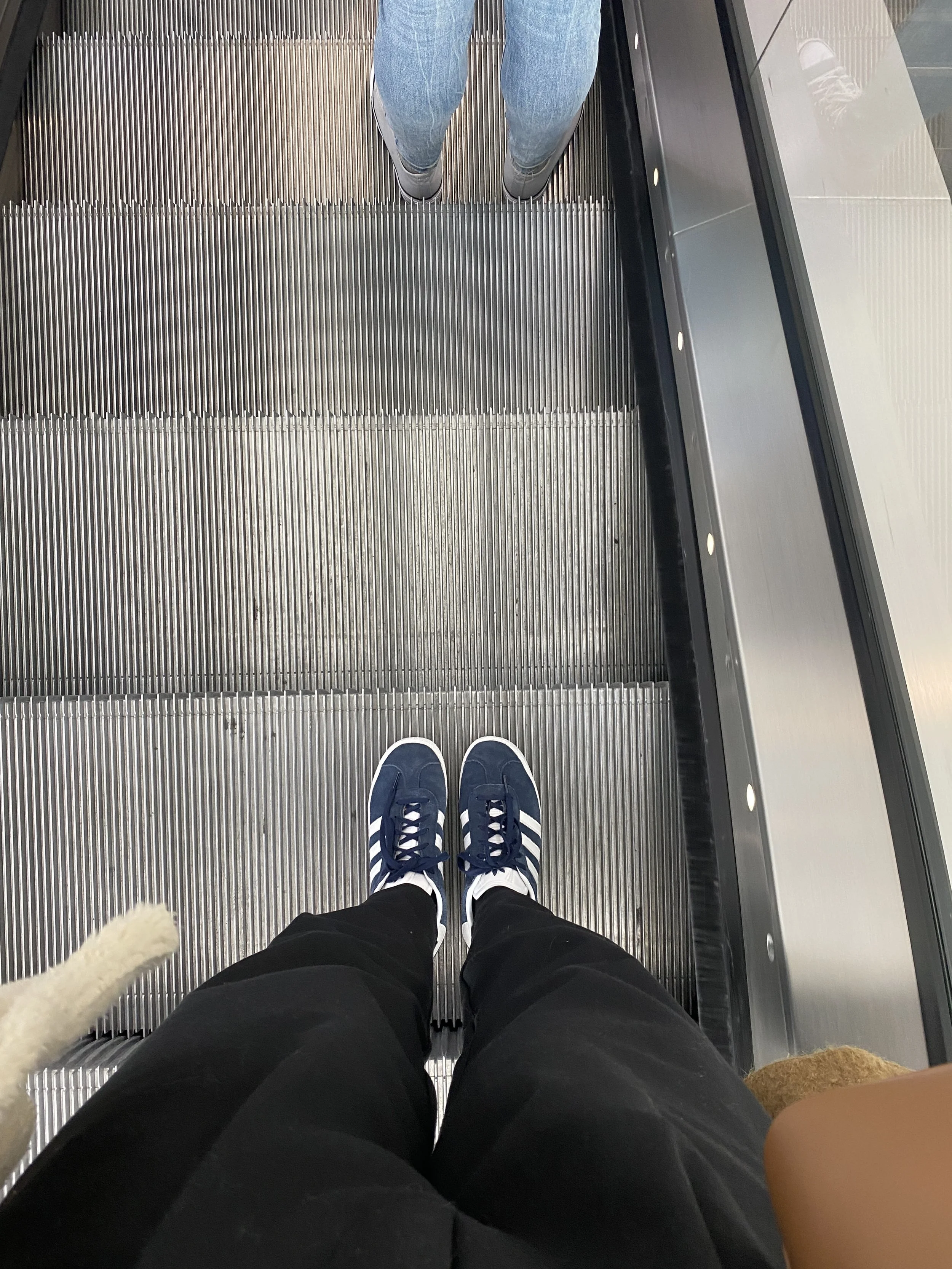 Person wearing blue sneakers and black pants standing on moving escalator, viewed from above.